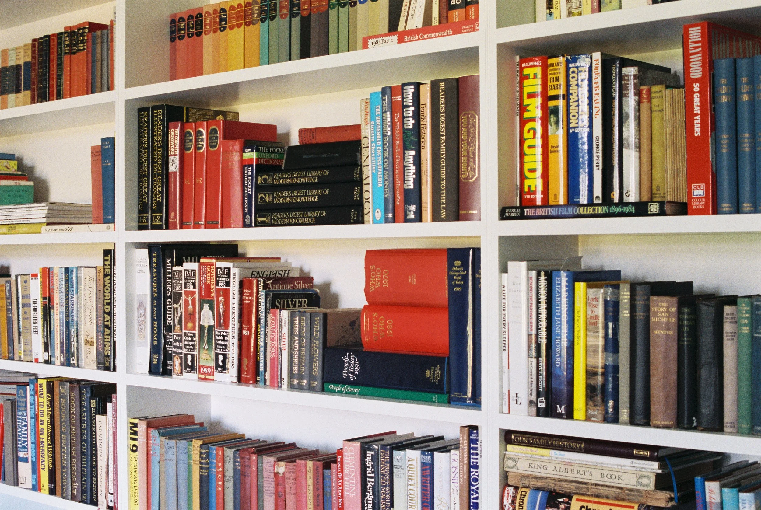 Bookshelves filled with various books and magazines, organized by color and size, in a library or bookstore setting.