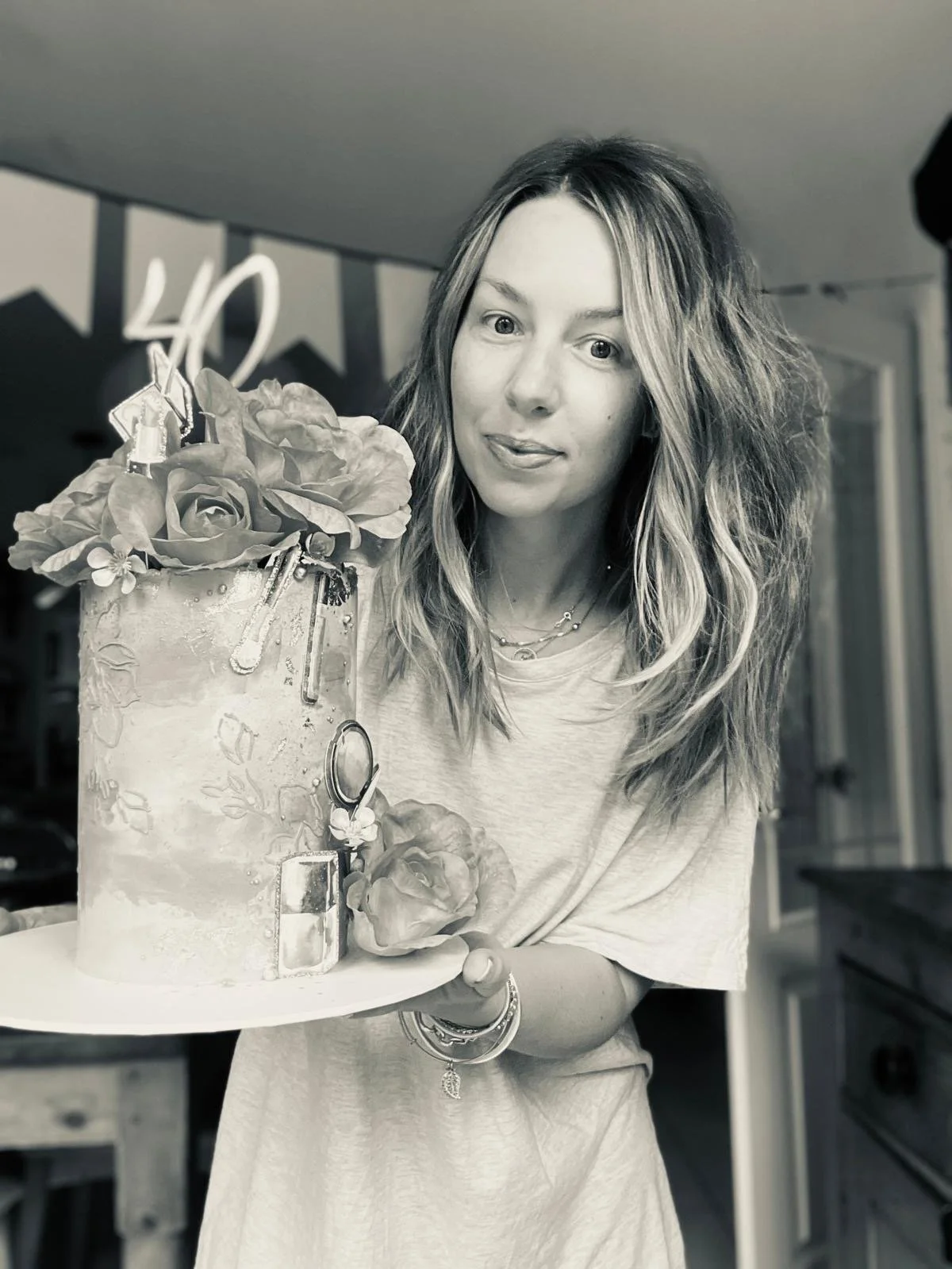 Woman with wavy hair holding a decorated cake with flowers on top.