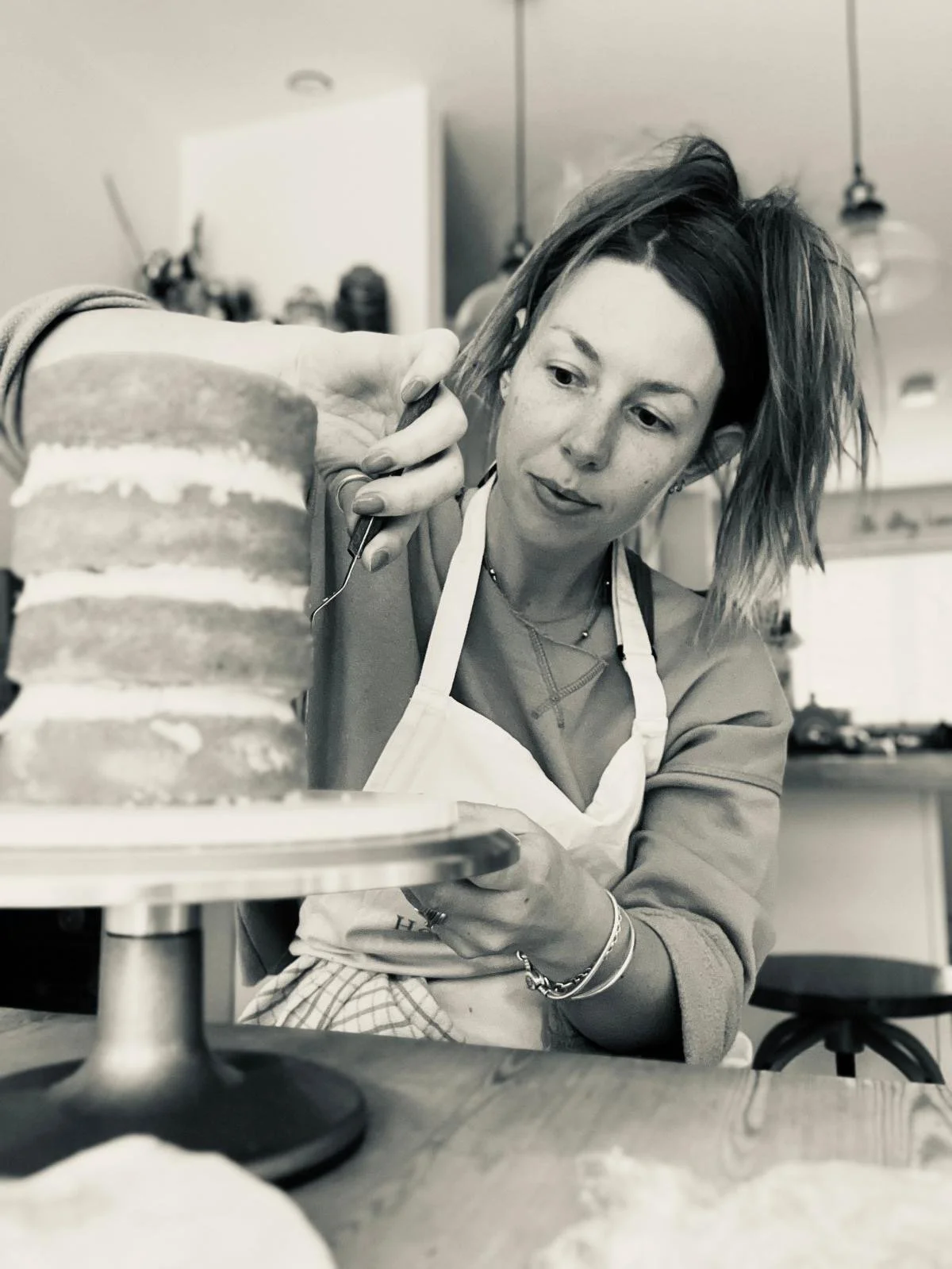 A woman decorating a layered cake in a kitchen.