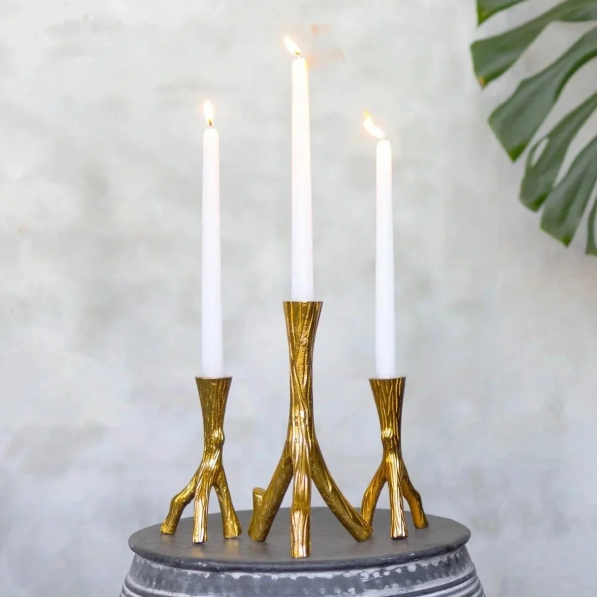 3 gold candle stands with white candles in them, all lit.