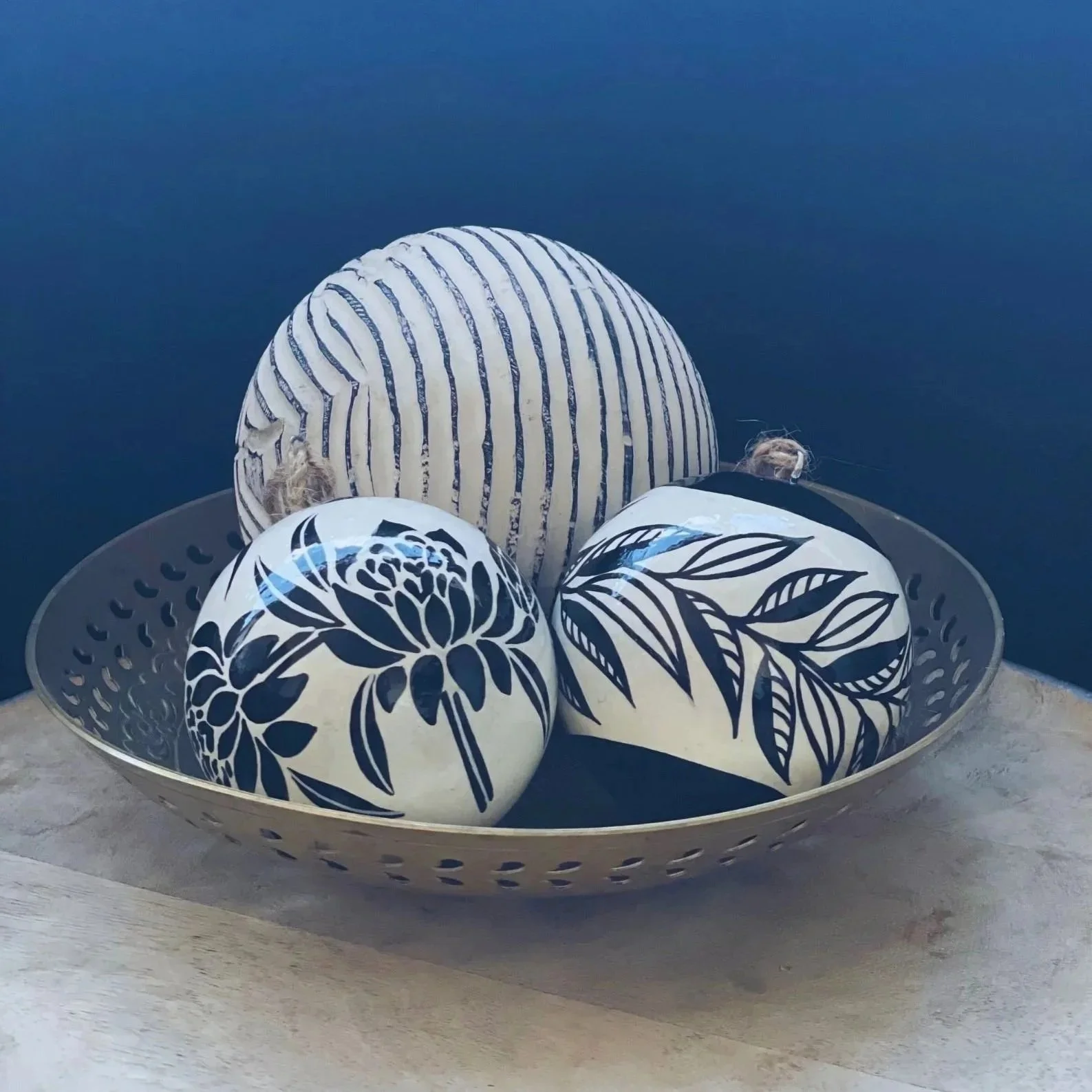 A brass bowl holding 2 floral baubles, against a dark background.