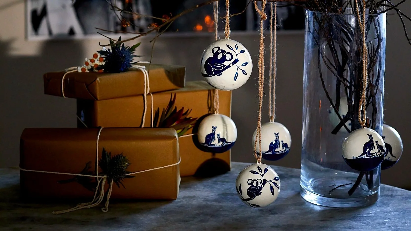 Hand-painted kangaroo and koala baubles hanging from branches in a vase beside wrapped gifts