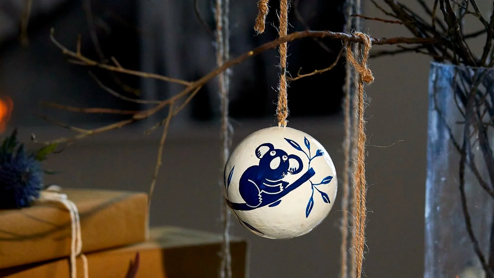 Hand-painted kangaroo and koala baubles hanging from branches in a vase beside wrapped gifts