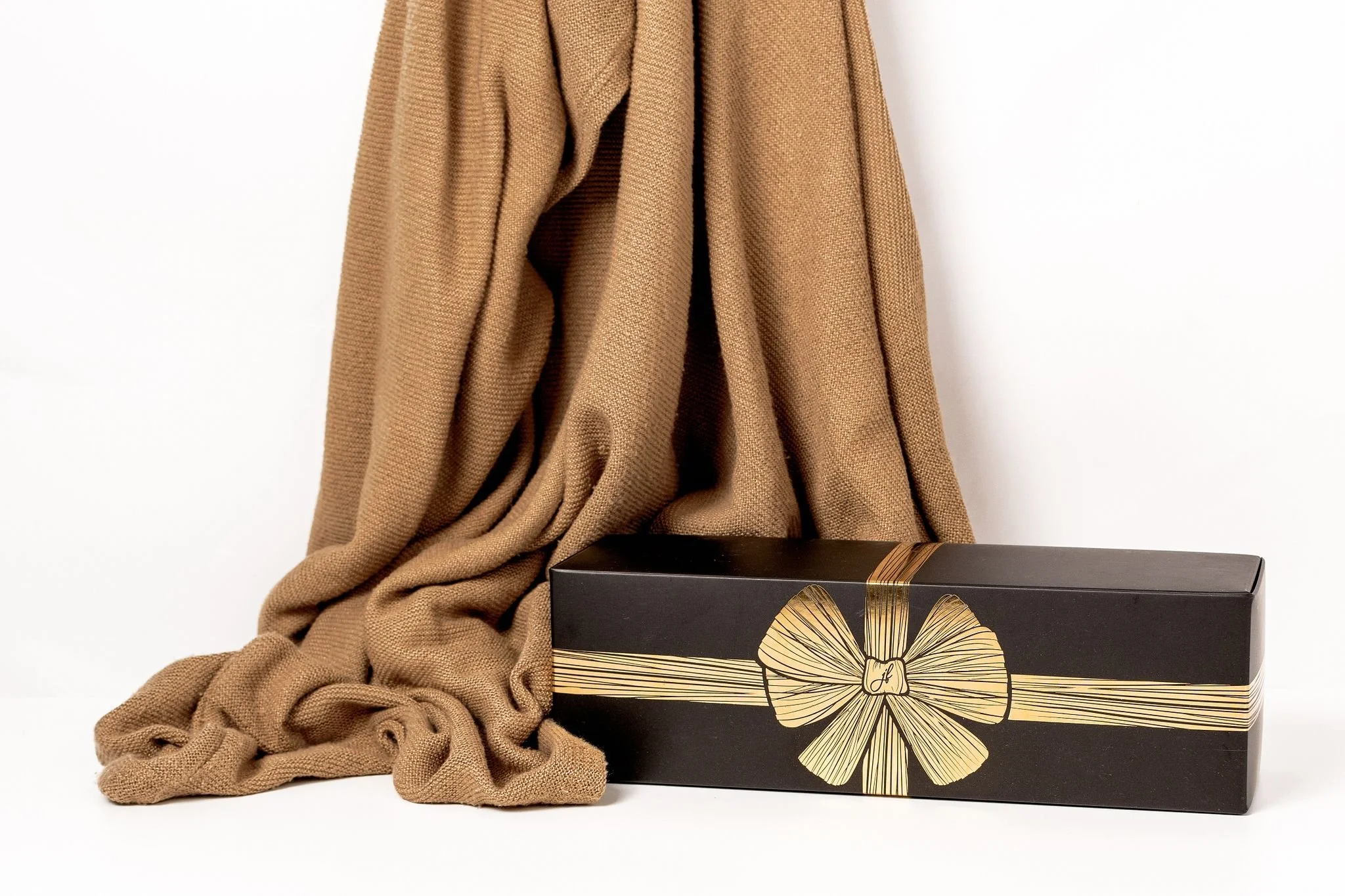 A brown blanket draped next to a black gift box with a gold ribbon design on its cover