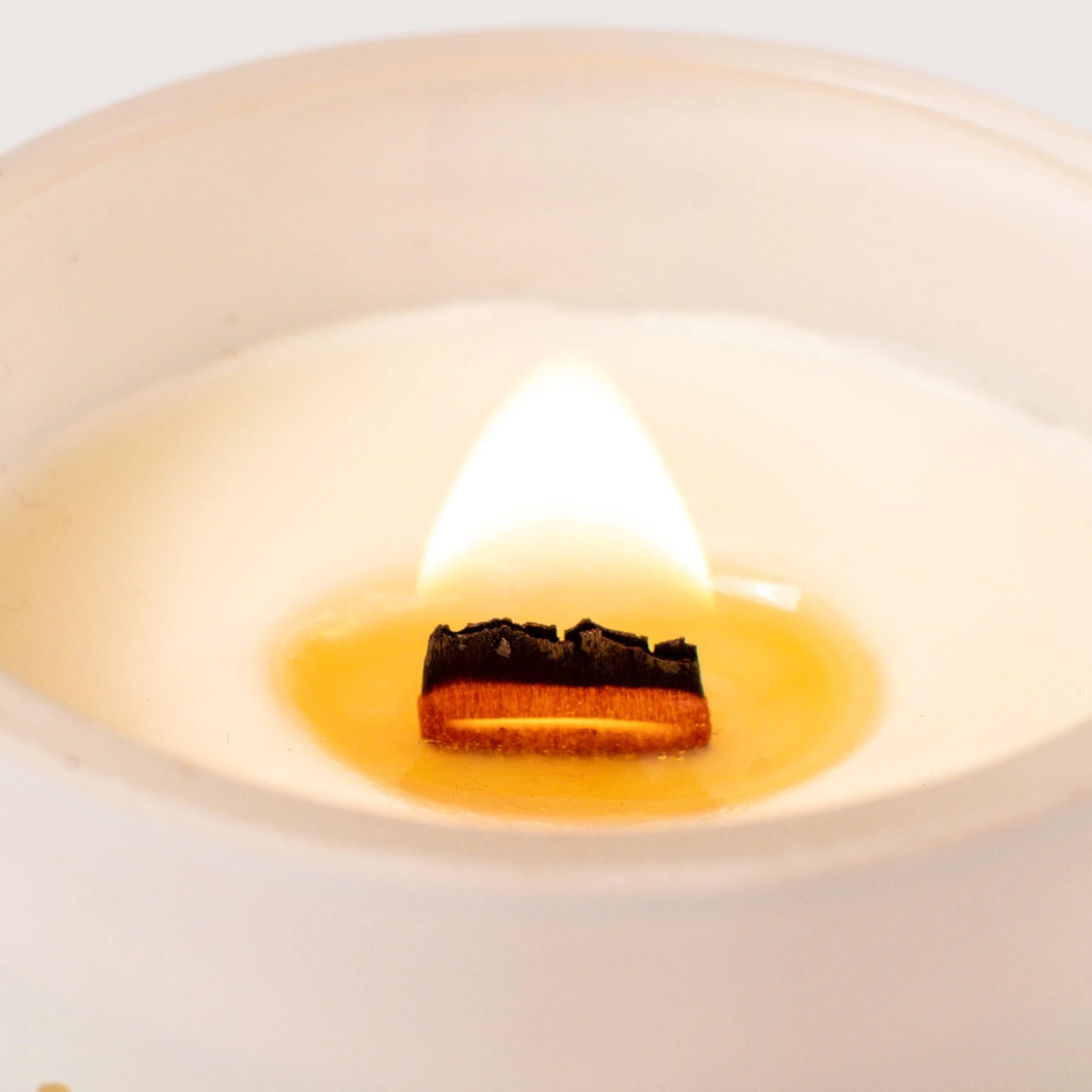 Close-up of a burning candle with a white exterior, revealing the wick and melted wax at the top.