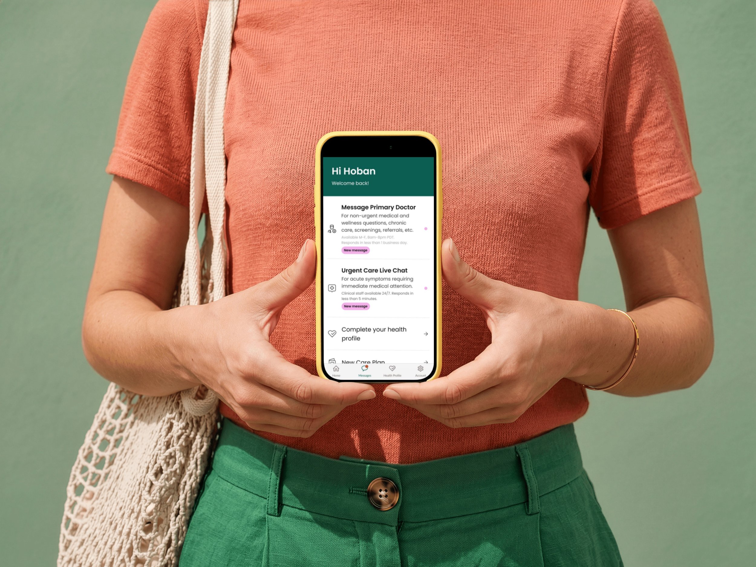 Person wearing a coral T-shirt and green pants holding a smartphone with a health app on the screen. The person also has a beige woven bag on their shoulder.