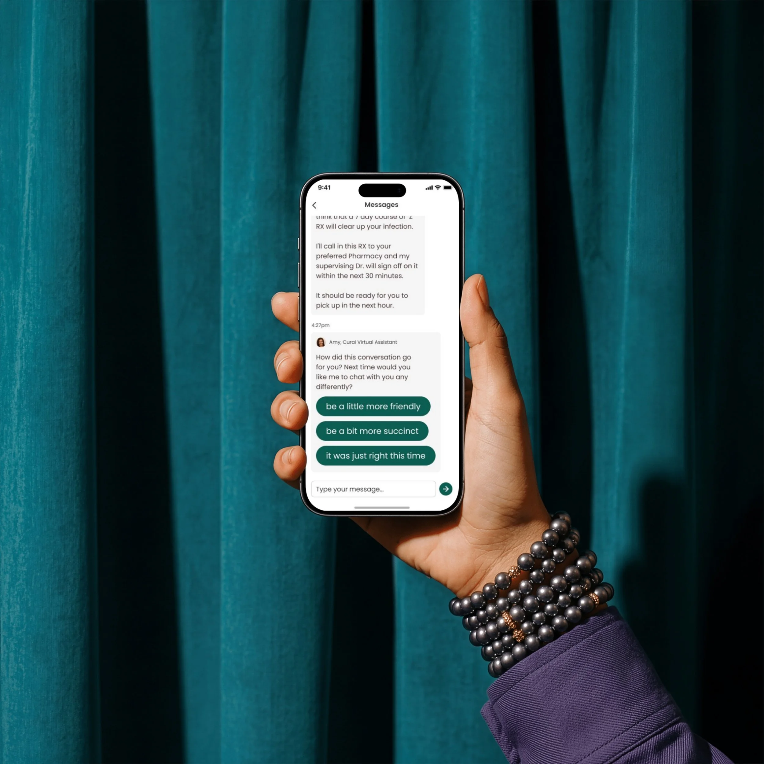 Close-up of a hand holding a smartphone with a messaging app open, against a teal curtain background. The person is wearing a purple sleeve and layered pearl bracelets.