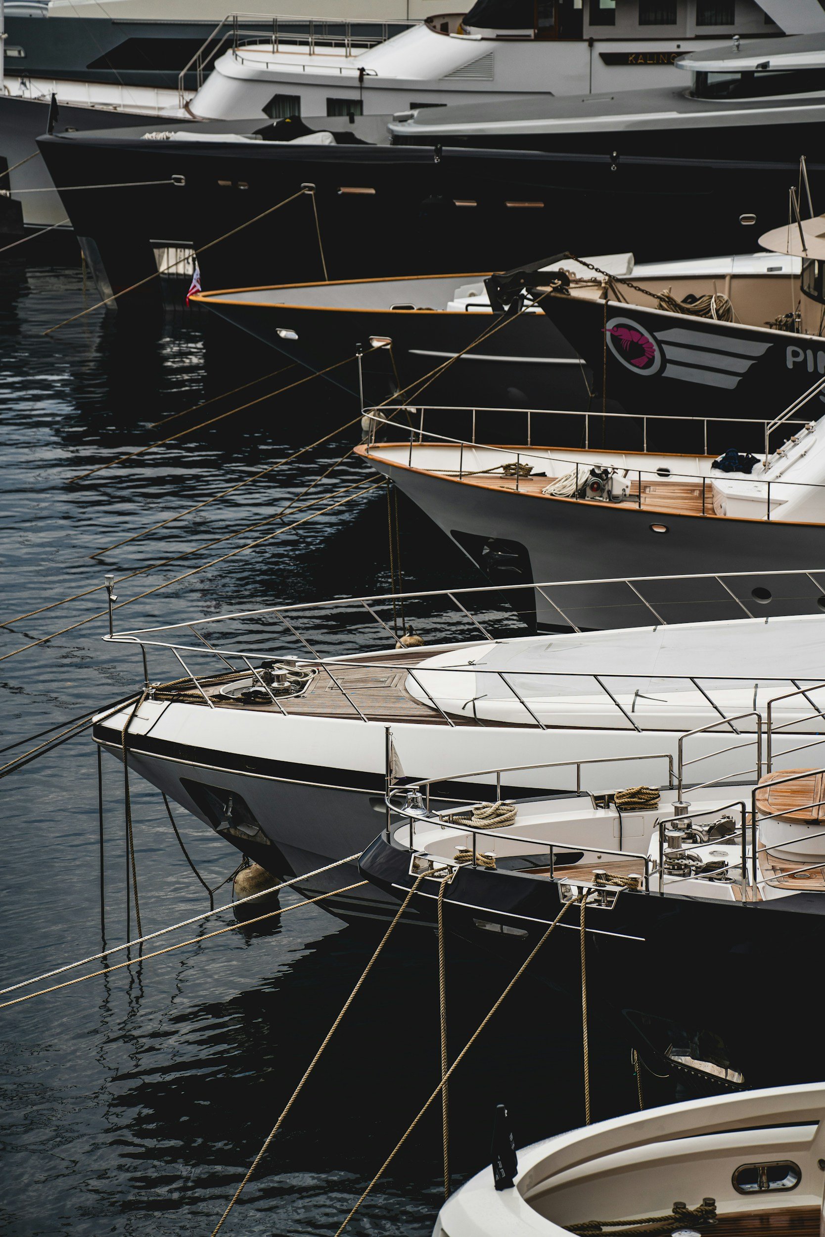 Groupe de yachts de luxe amarrés dans un port, avec des cordages visibles et l'eau en dessous.
