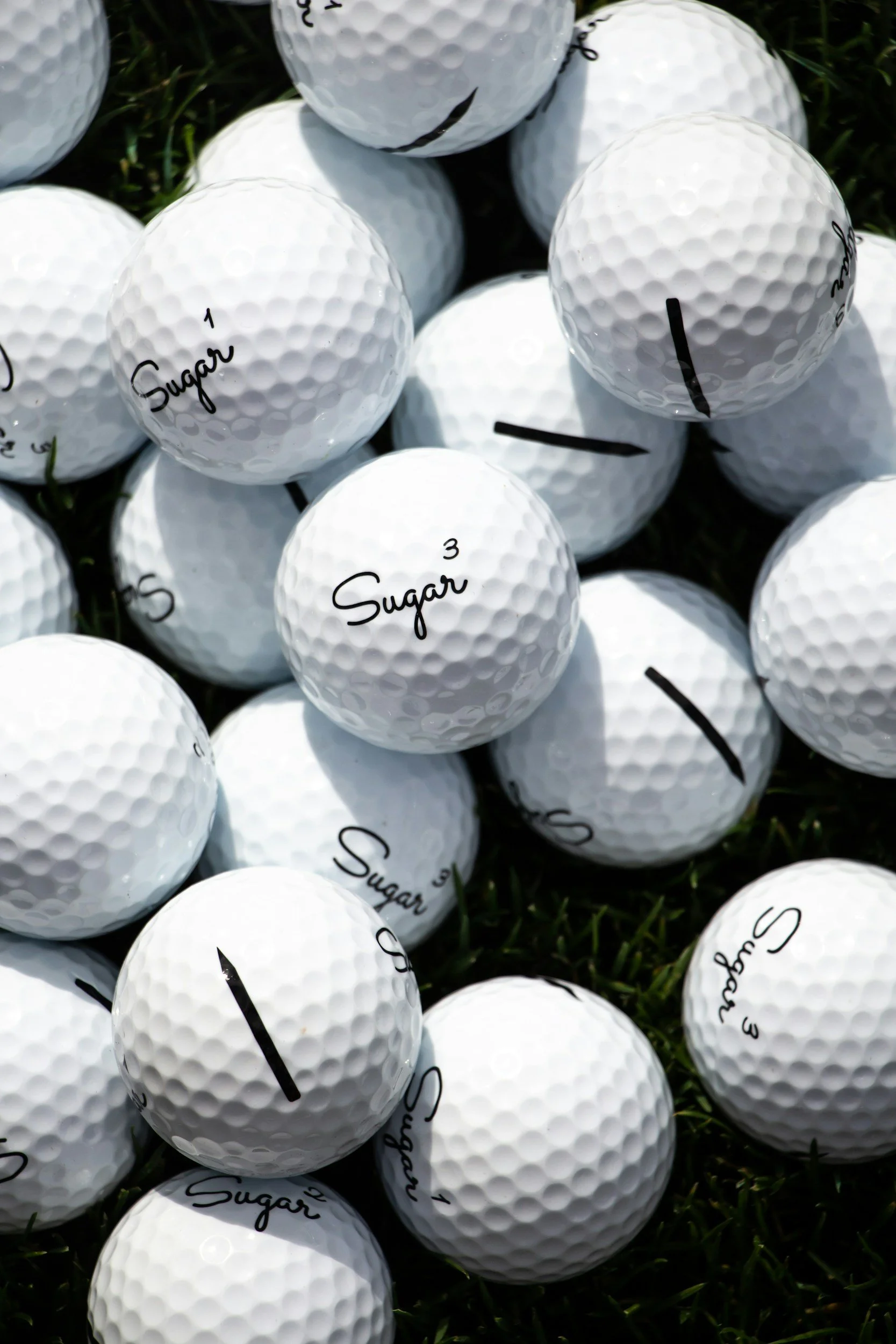 Boules de golf blanches avec l'inscription 'Sugar 1' et autres numéros, disposées sur de l'herbe verte.