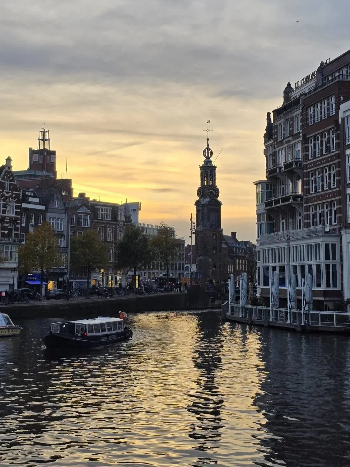 Sunset over a canal in a European city, with boats docked in the water and historic buildings along the street.