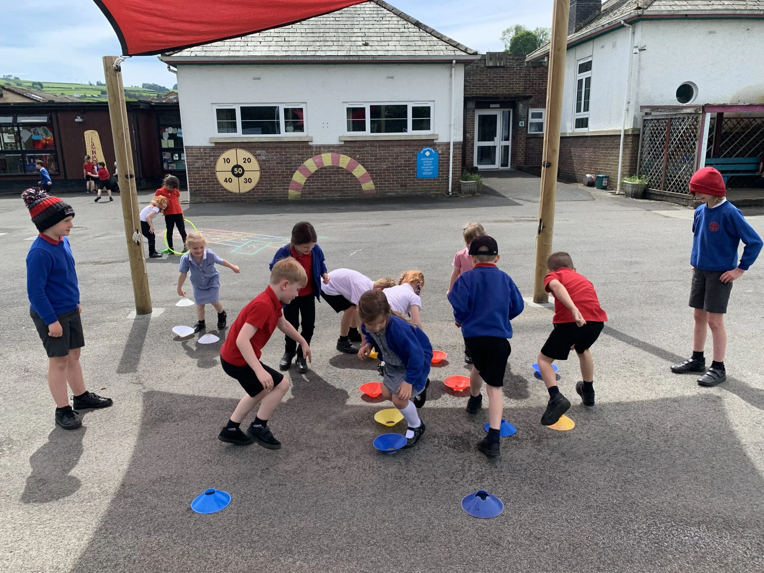 Children playing outdoors on a school yard with cones and educational wall decorations, under cloudy sky.