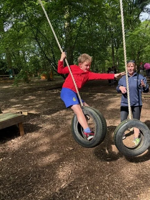 Child swinging on tire swings in a park with trees in the background.
