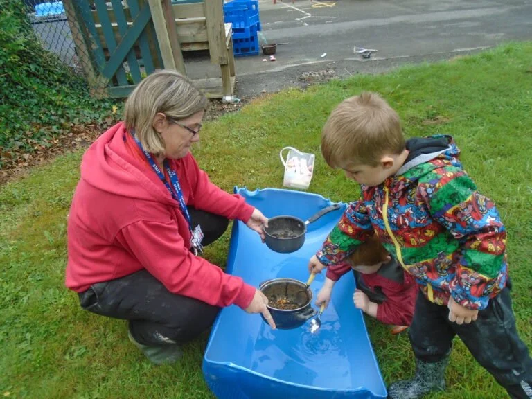 Adult and children playing with water in a sandbox outdoors