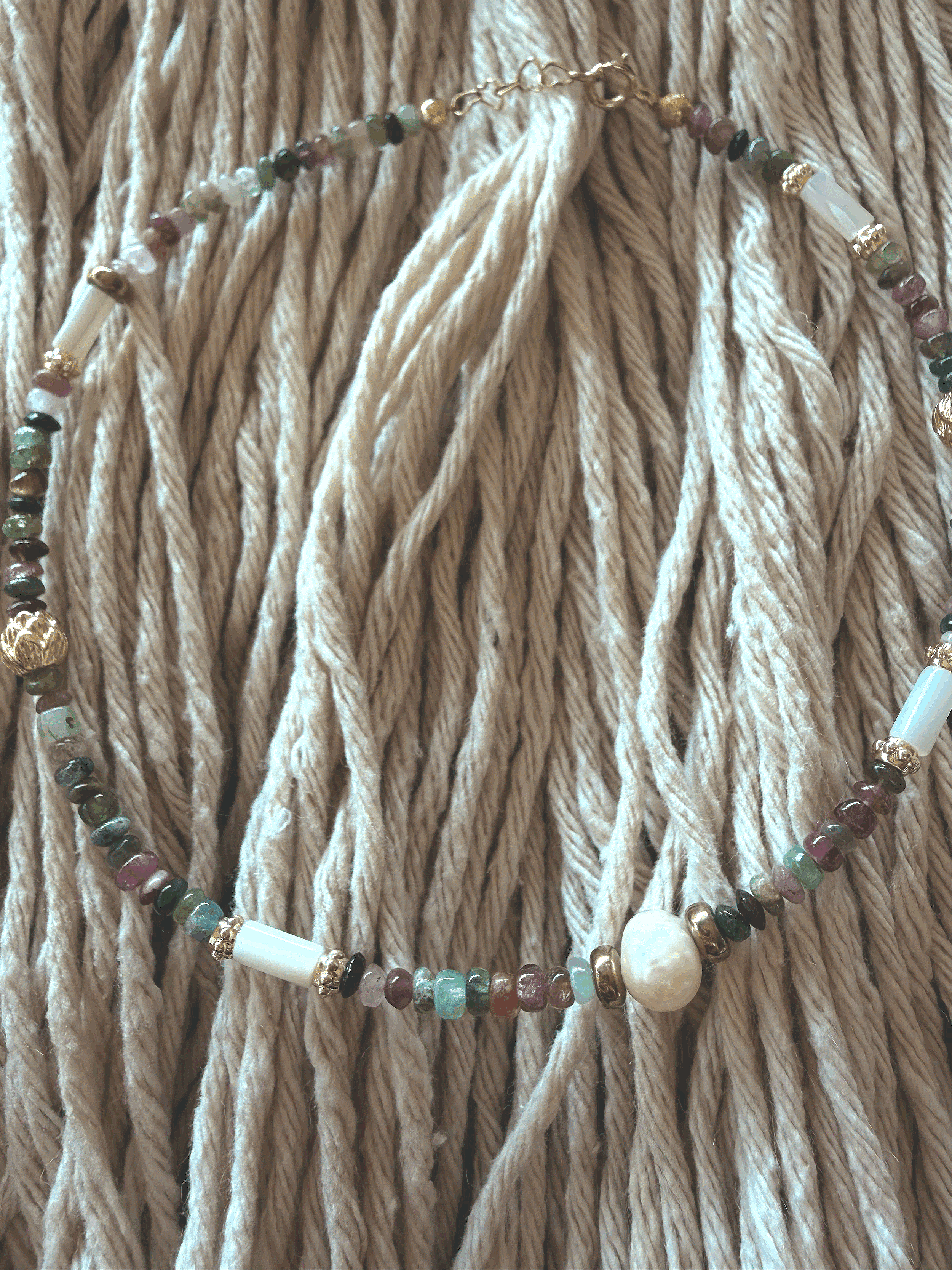 Close-up of the Midnight Tourmaline anklet on woven rope, showing multicolor tourmaline chip beads, gold-tone spacers, and a freshwater pearl accent