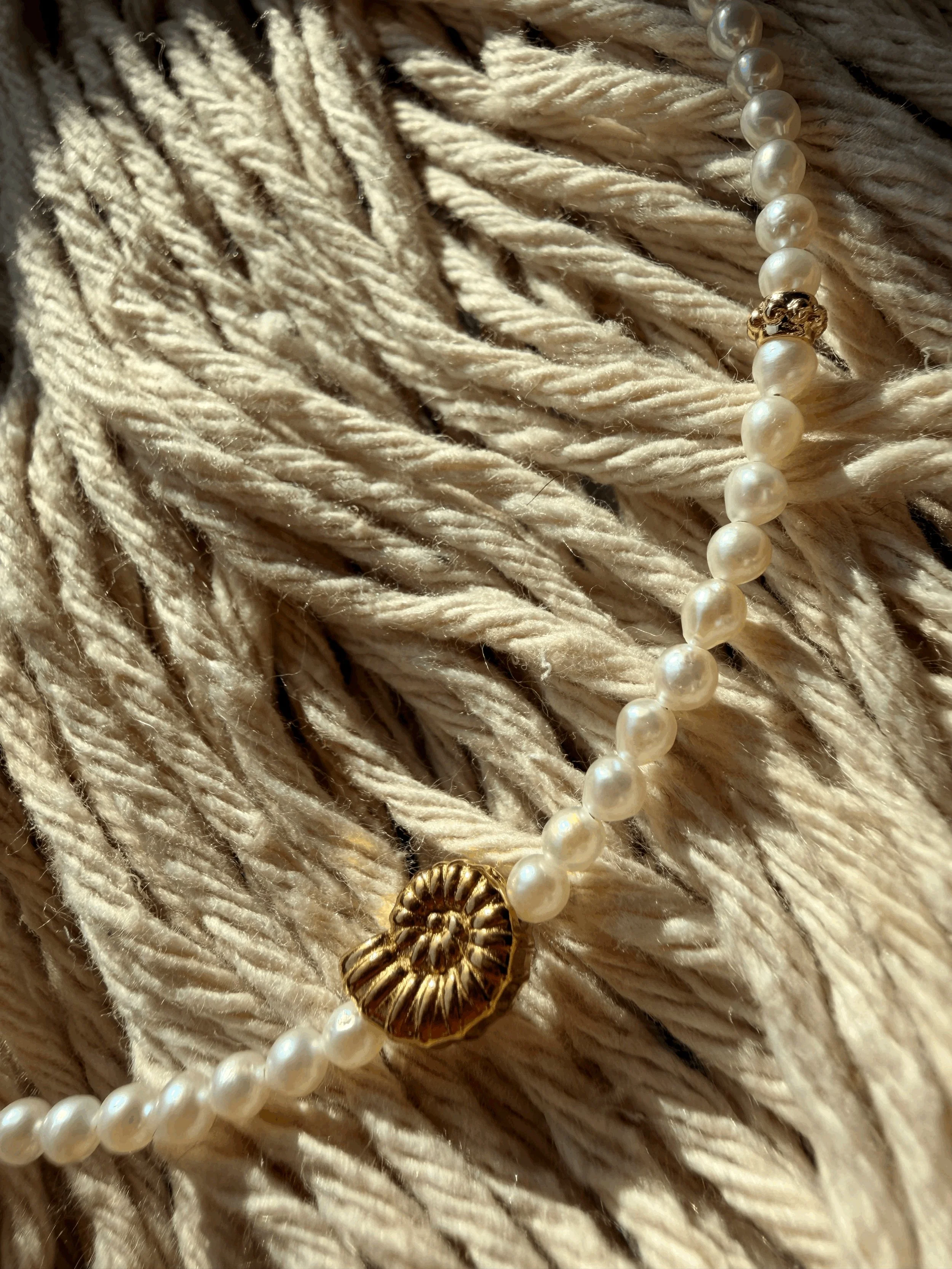 Close-up of the Pearl Infinity Anklet's freshwater pearls and gold nautilus shell charm, resting on cream rope.
