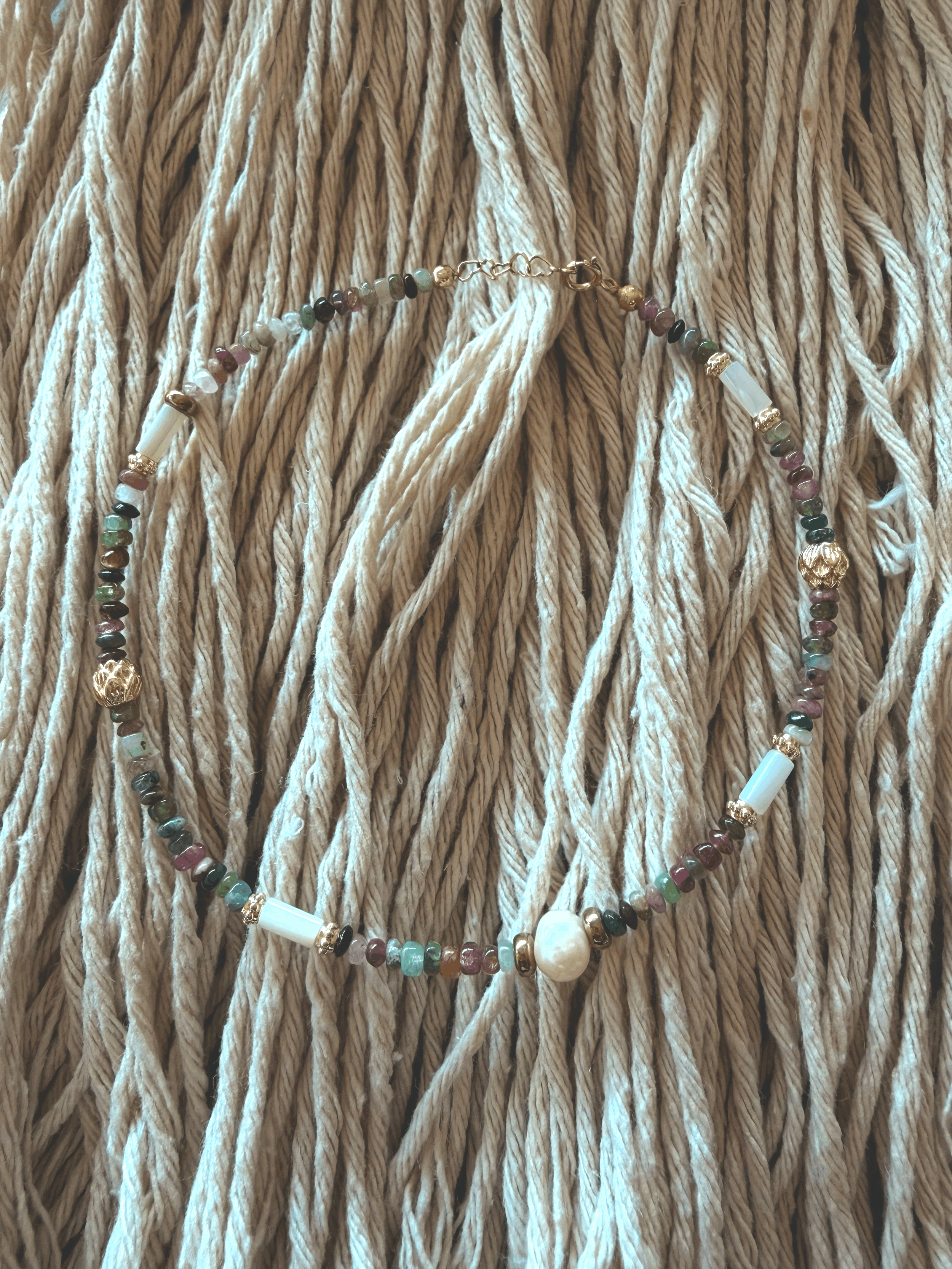Midnight Tourmaline anklet laid on woven rope, featuring multicolor tourmaline chip beads, gold-tone accent beads, and a freshwater pearl centerpiece