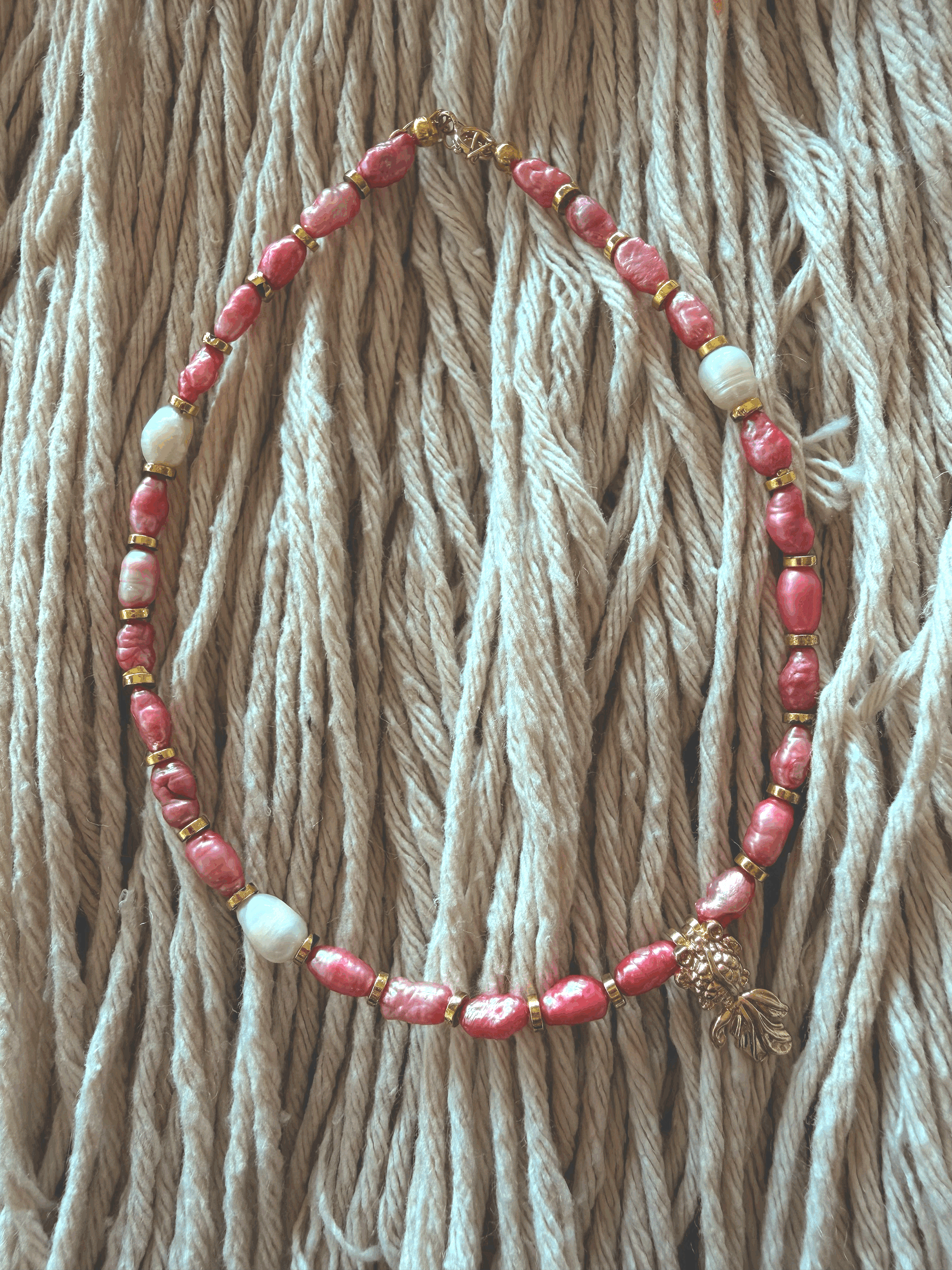 Elegant Pink anklet laid out on woven rope, featuring pink-dyed natural pearls, gold spacers, a white pearl accent, and a gold fish charm.