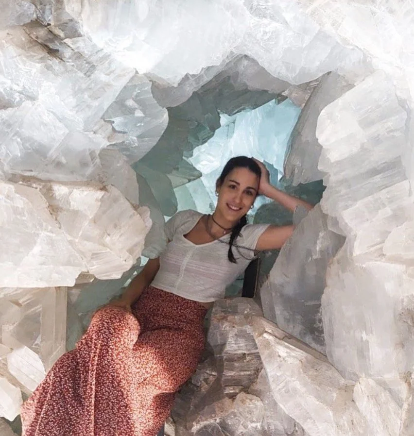 A woman sitting inside a large ice cave, smiling and resting her head on her hand.
