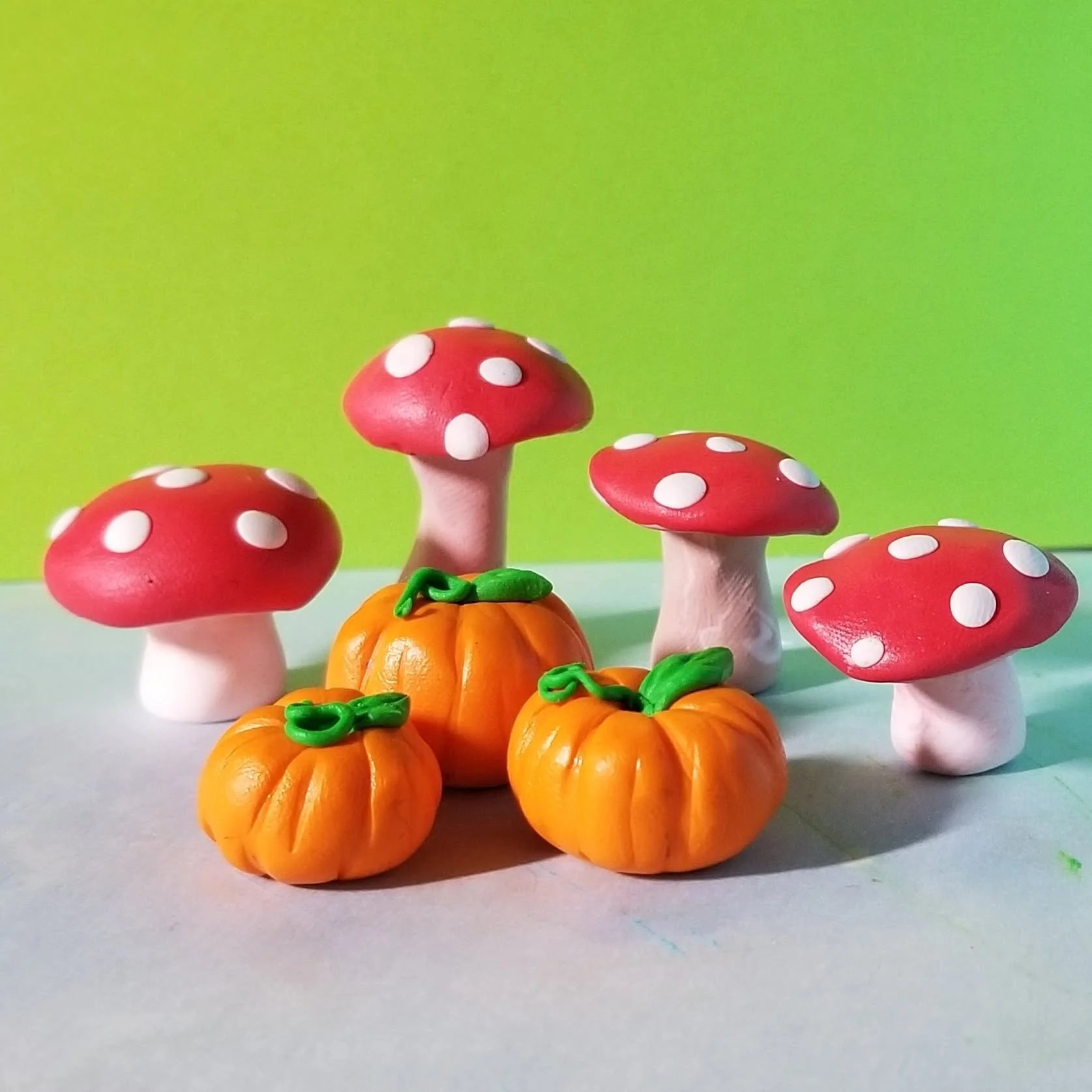 Plastic pumpkin decorations with red and white polka dot mushrooms and green vines on a white surface with a green background.