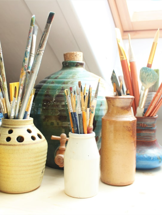 Assorted paintbrushes and pottery vases on a table.