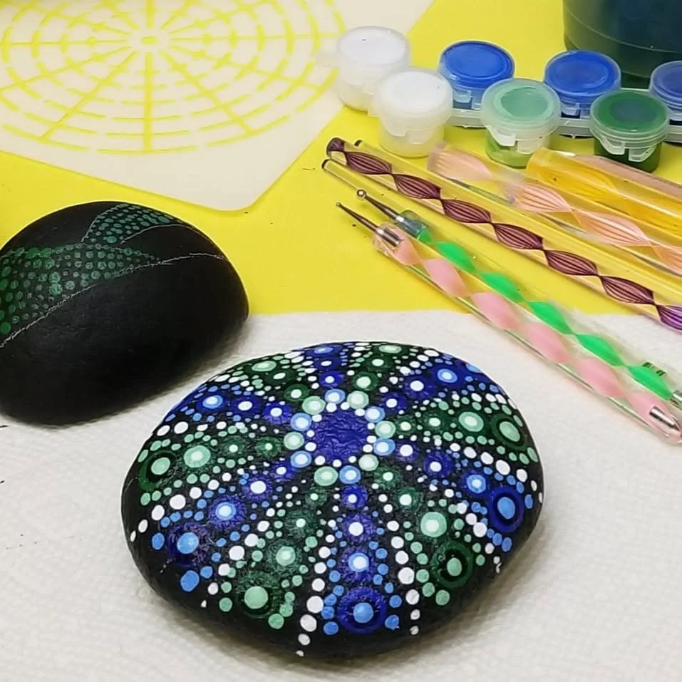 Painted rocks with dot art designs, nail polish bottles, dotting tools, and a color wheel for rock painting.