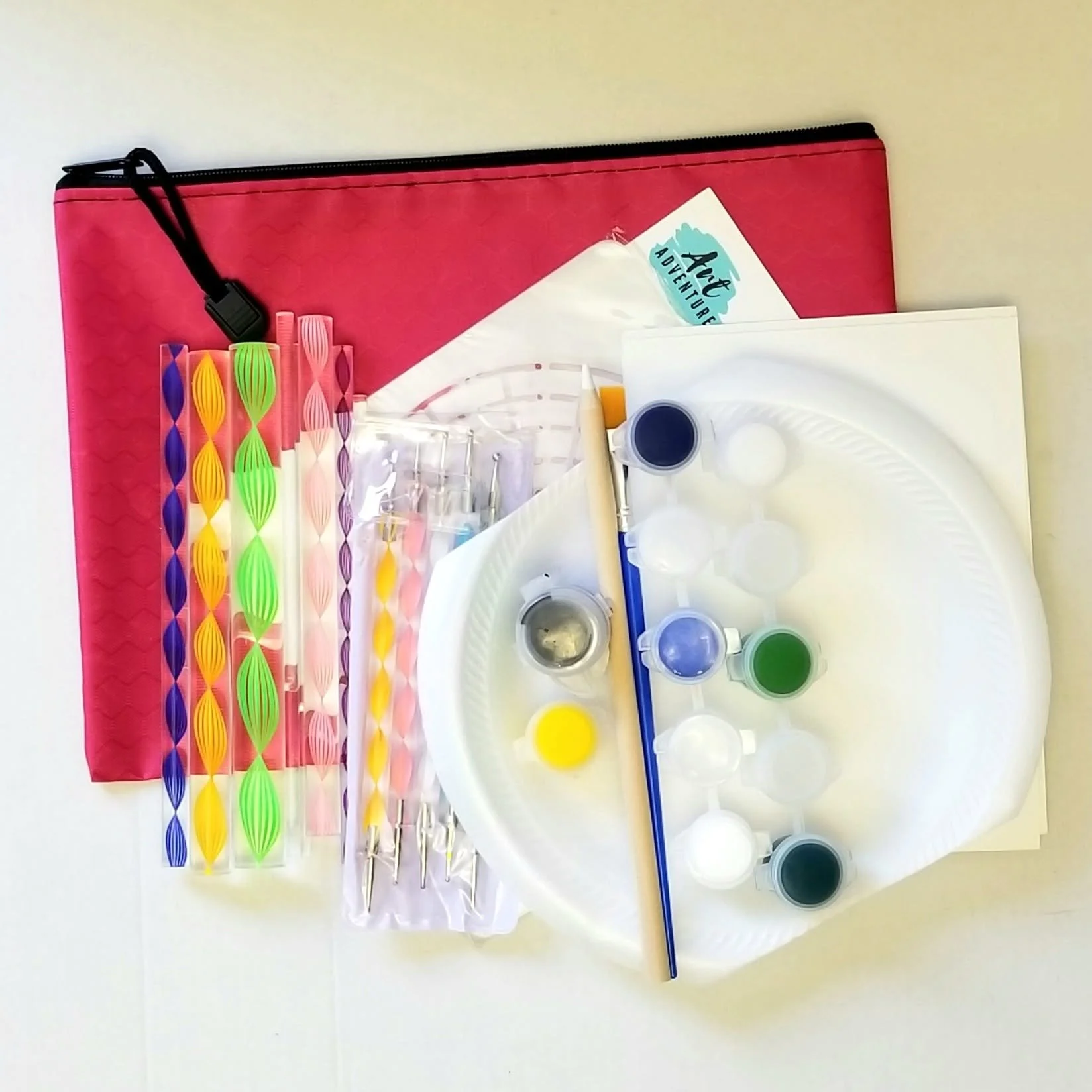 Set of colorful glass stirring rods, a sample holder with pipettes, and an art adventure booklet on a white surface.
