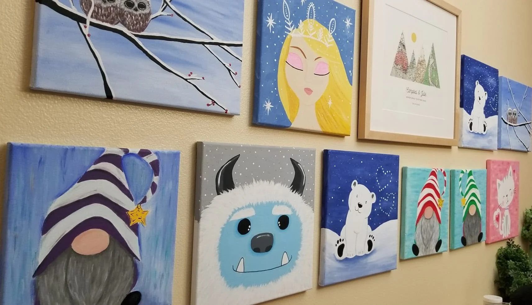 A wall decorated with various colorful, cartoon-style paintings and illustrations of animals, a fantasy princess, and holiday themes, arranged in a gallery style.