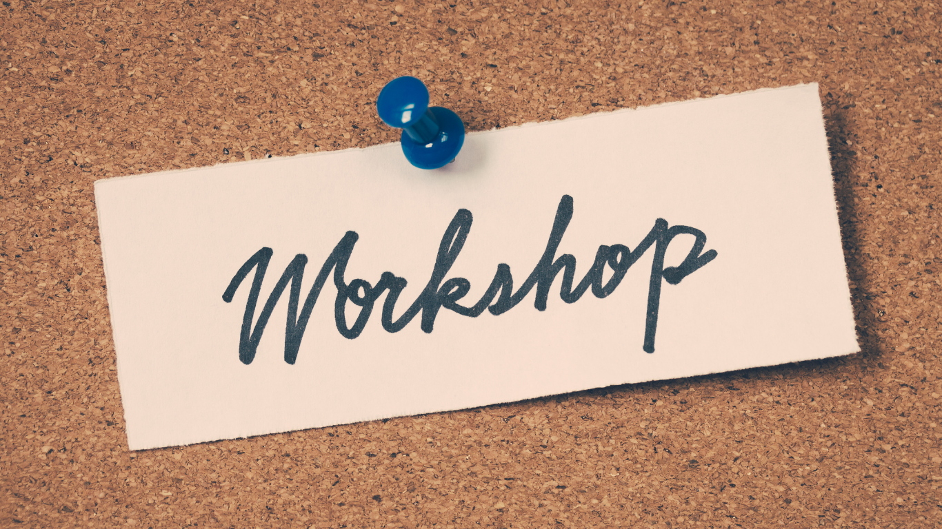 A white paper with the word 'Workshop' written in black cursive, pinned to a corkboard with a blue pushpin.
