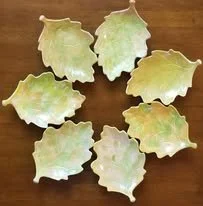 Eight brass leaf-shaped dishes arranged in a circle on a wooden surface.