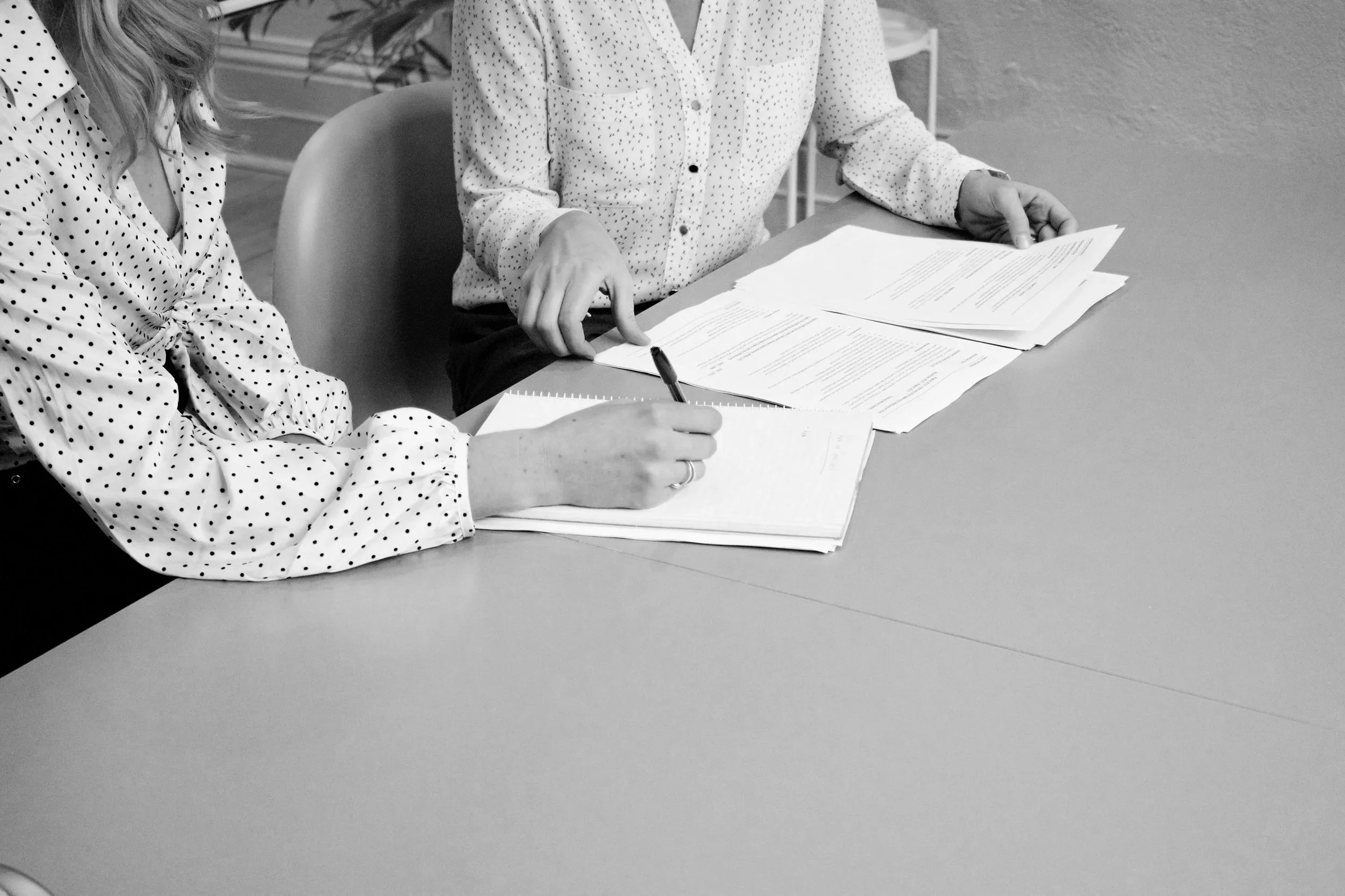 Two women overlook and edit a stack of papers.