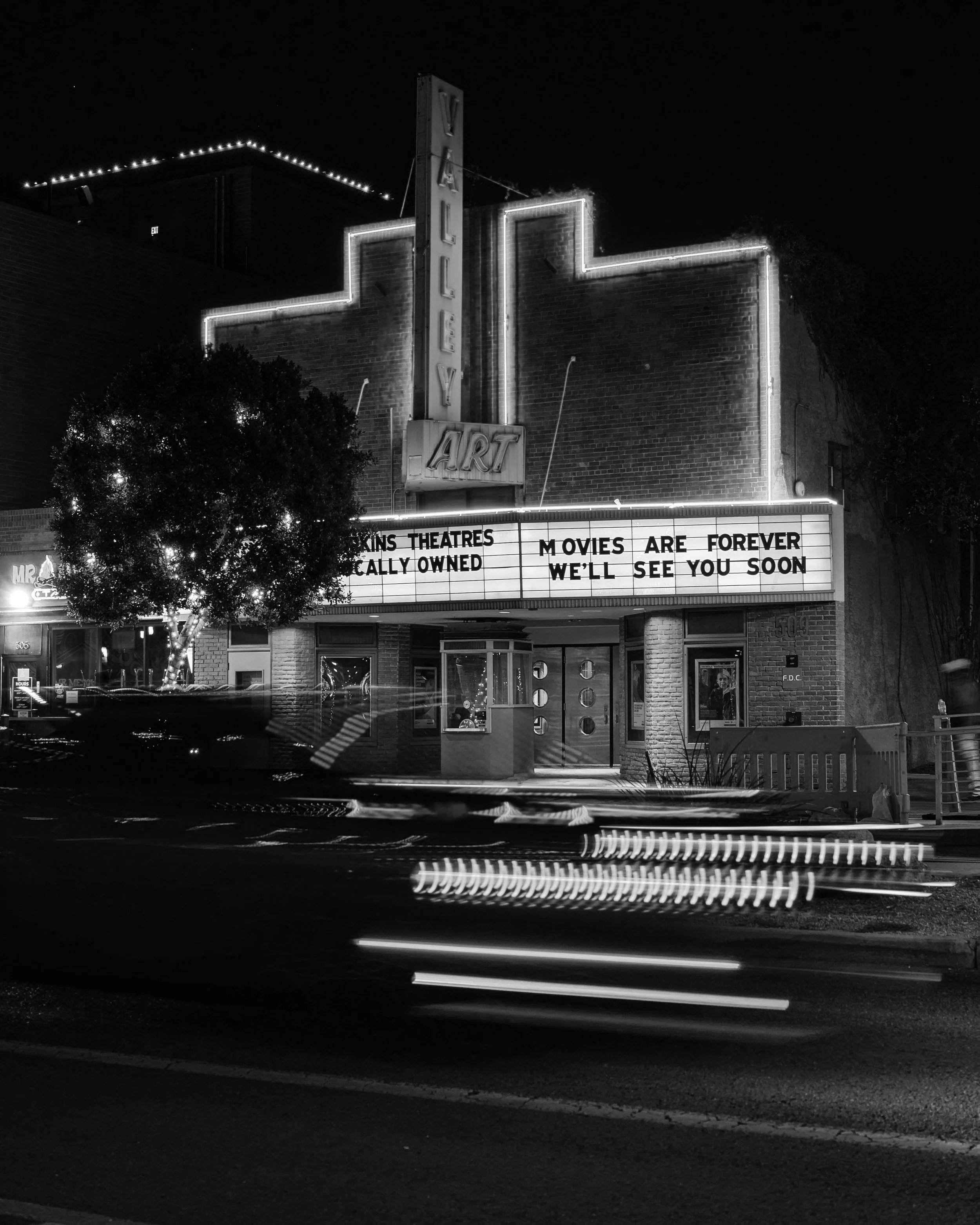 The outside of movie theater marquee at night in black and white.