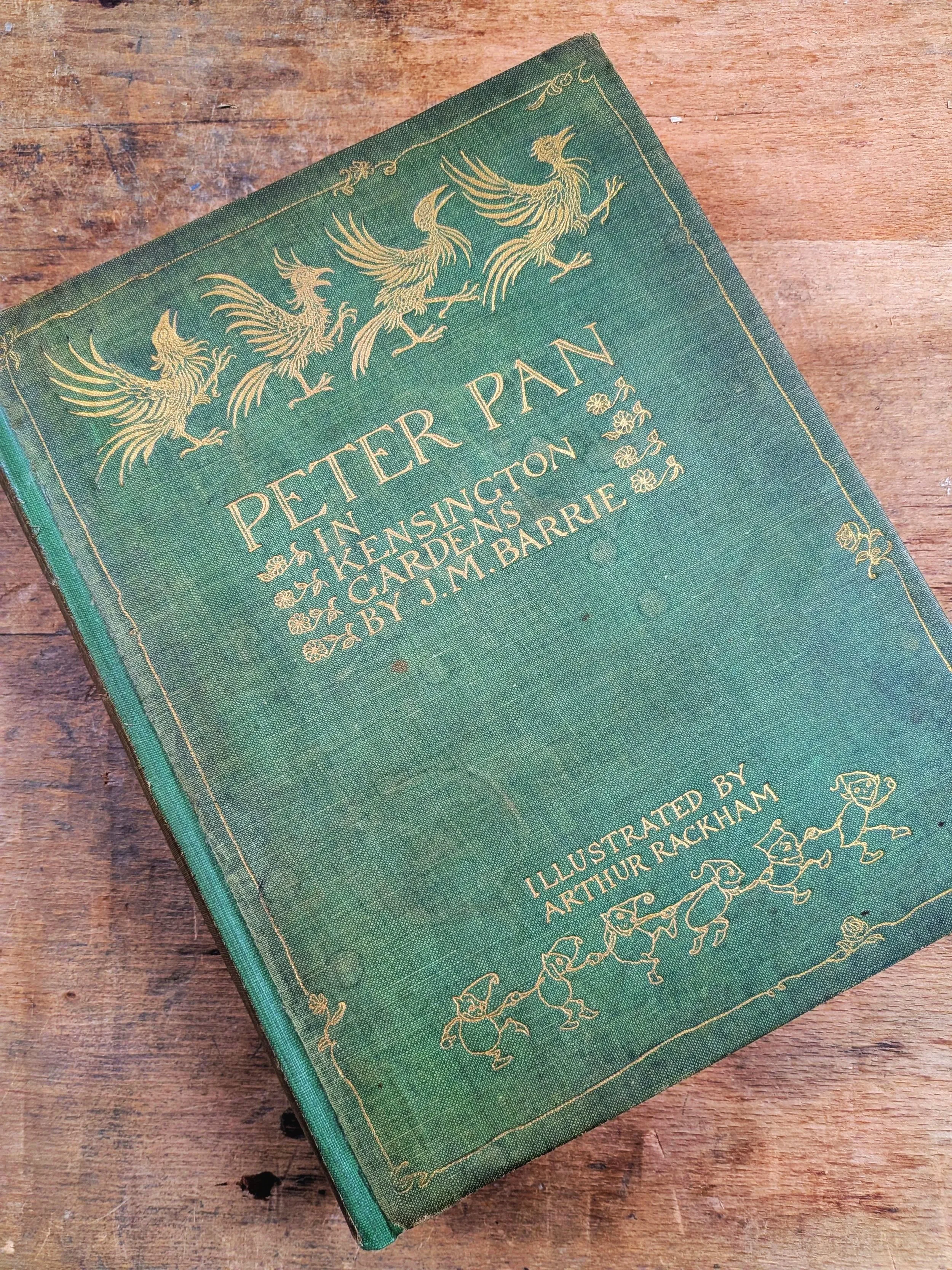 A vintage green hardcover book titled "Peter Pan" by J. M. Barrie, illustrated by Arthur Rackham, lying on a wooden surface. This is an example of excellent repair and restoration work that involved page repairs and a technique called rebacking.