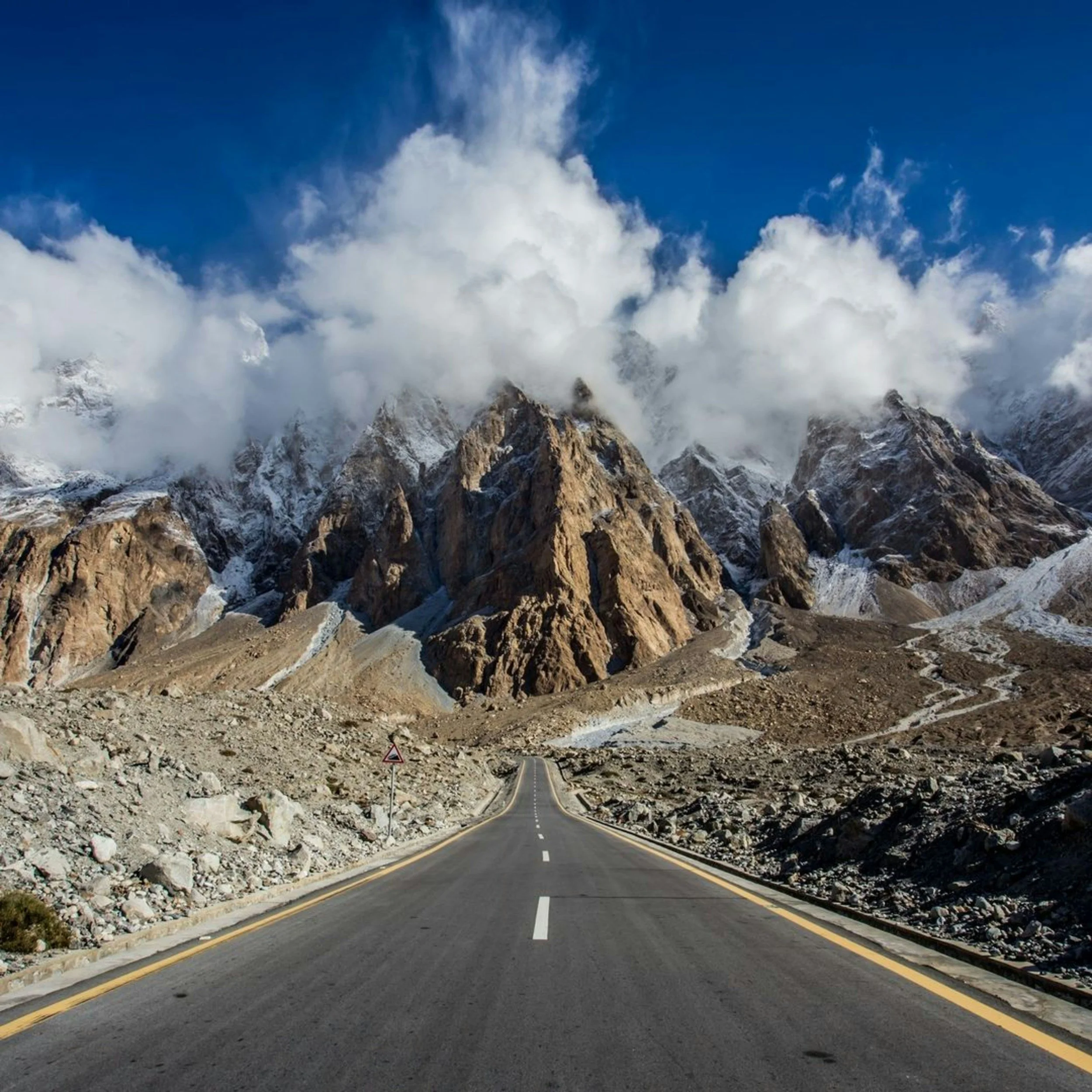 A mountain road surrounded by rocky terrain and snow-capped peaks, with steep mountain walls and a clear sky.