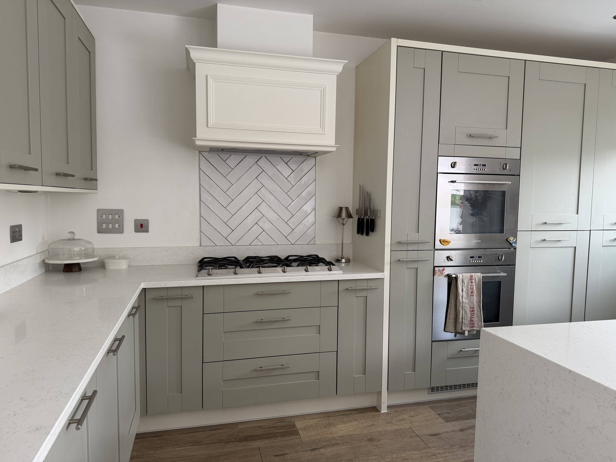 Modern kitchen with white cabinets, a built-in oven, a gas stove, a white range hood, and a marble backsplash.