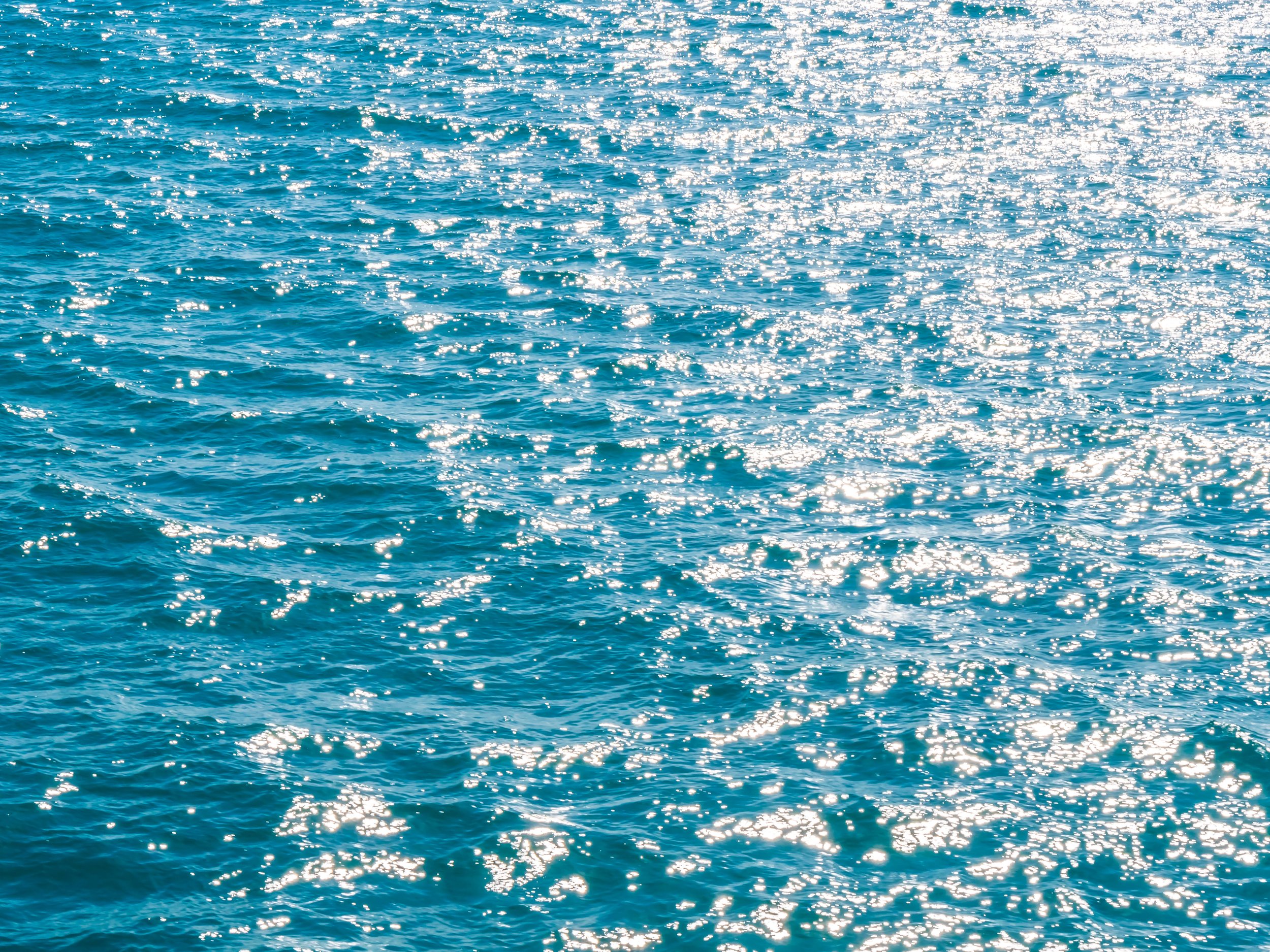 Vista de un océano con agua azul y reflejos de luz solar en la superficie.