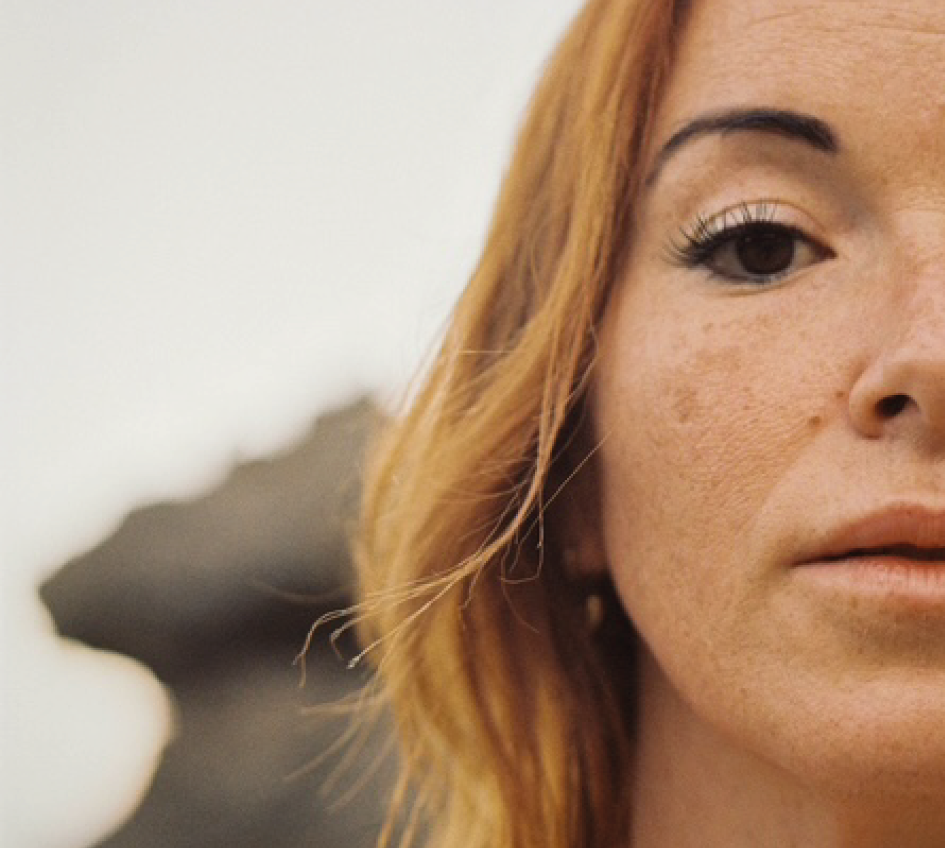 Primer plano del rostro de una mujer con cabello rubio rizado y piel con pecas, mostrando su ojo y parte de su mejilla.
