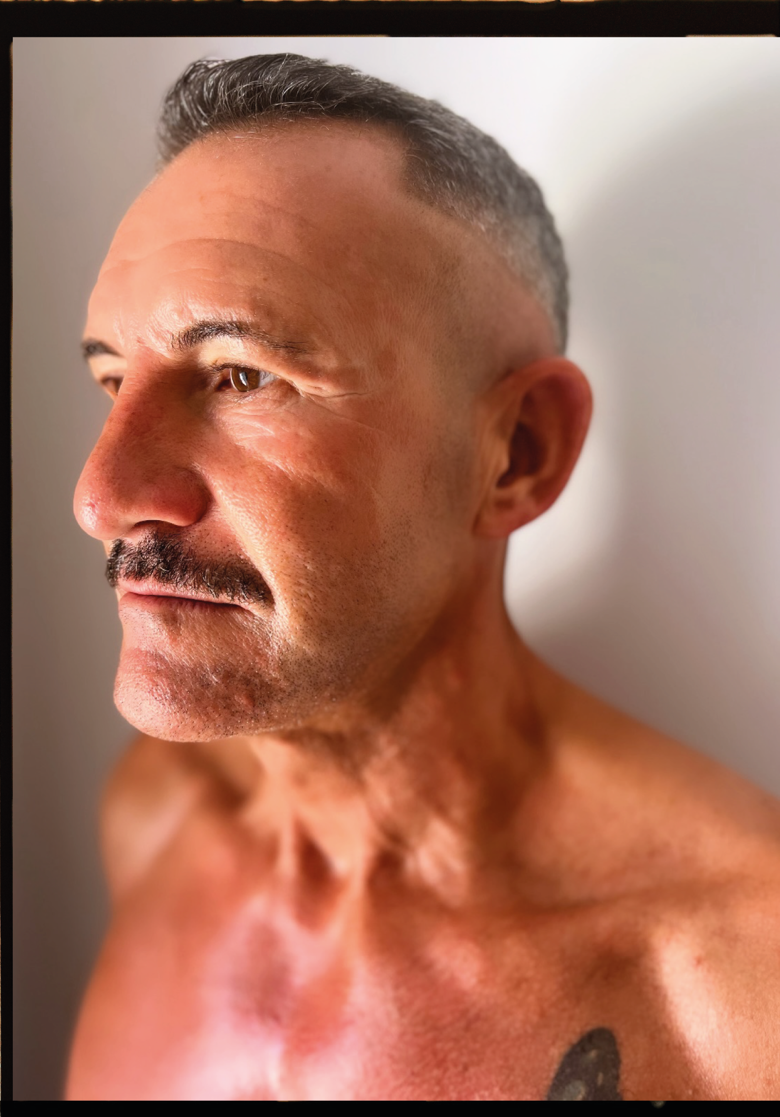 Retrato de un hombre con barba, cabello corto y canoso, con piel bronceada y lleno de tatuajes, centrado en su rostro y parte del torso.