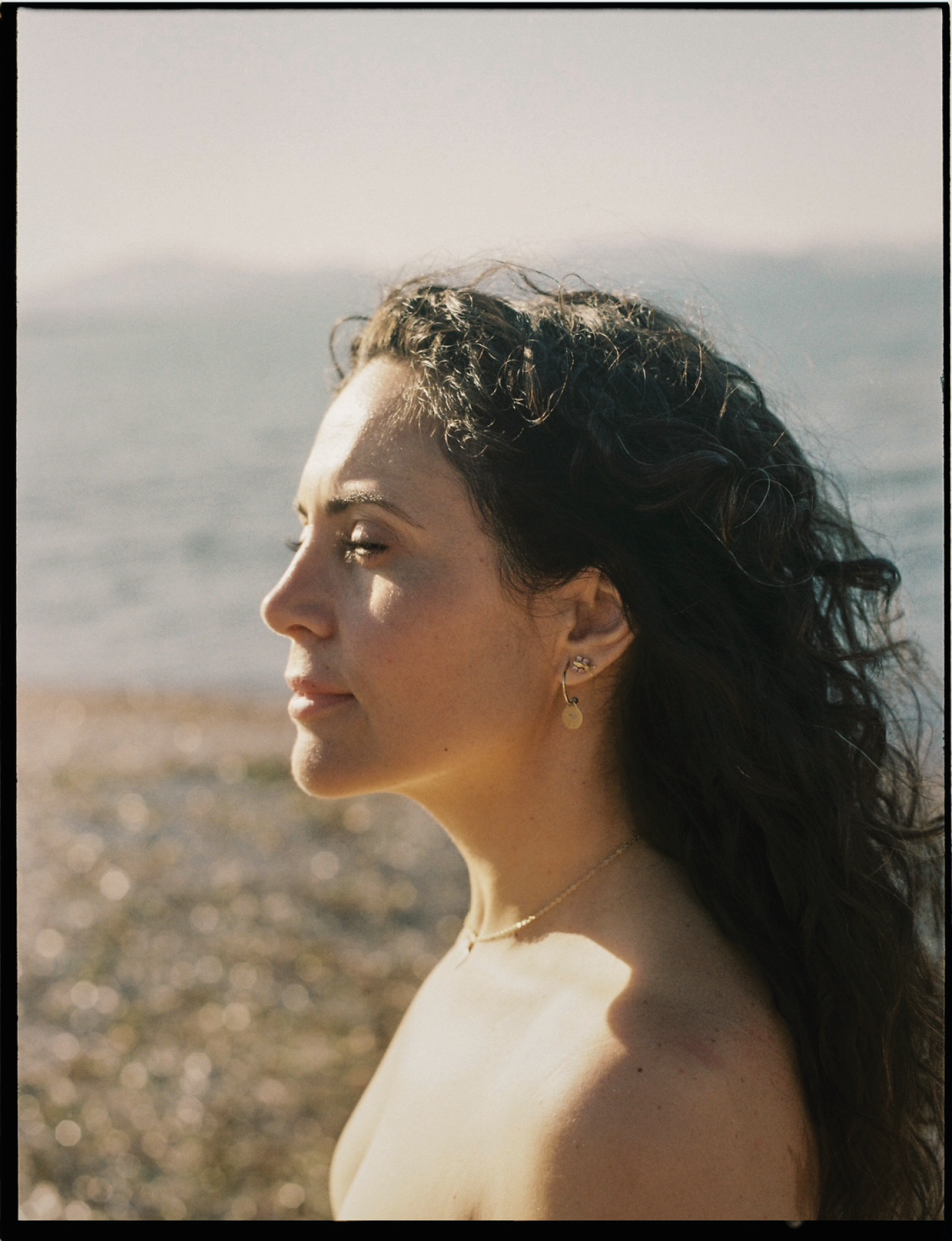 Retrato de una mujer con cabello rizado en un fondo de playa y mar, durante el día.