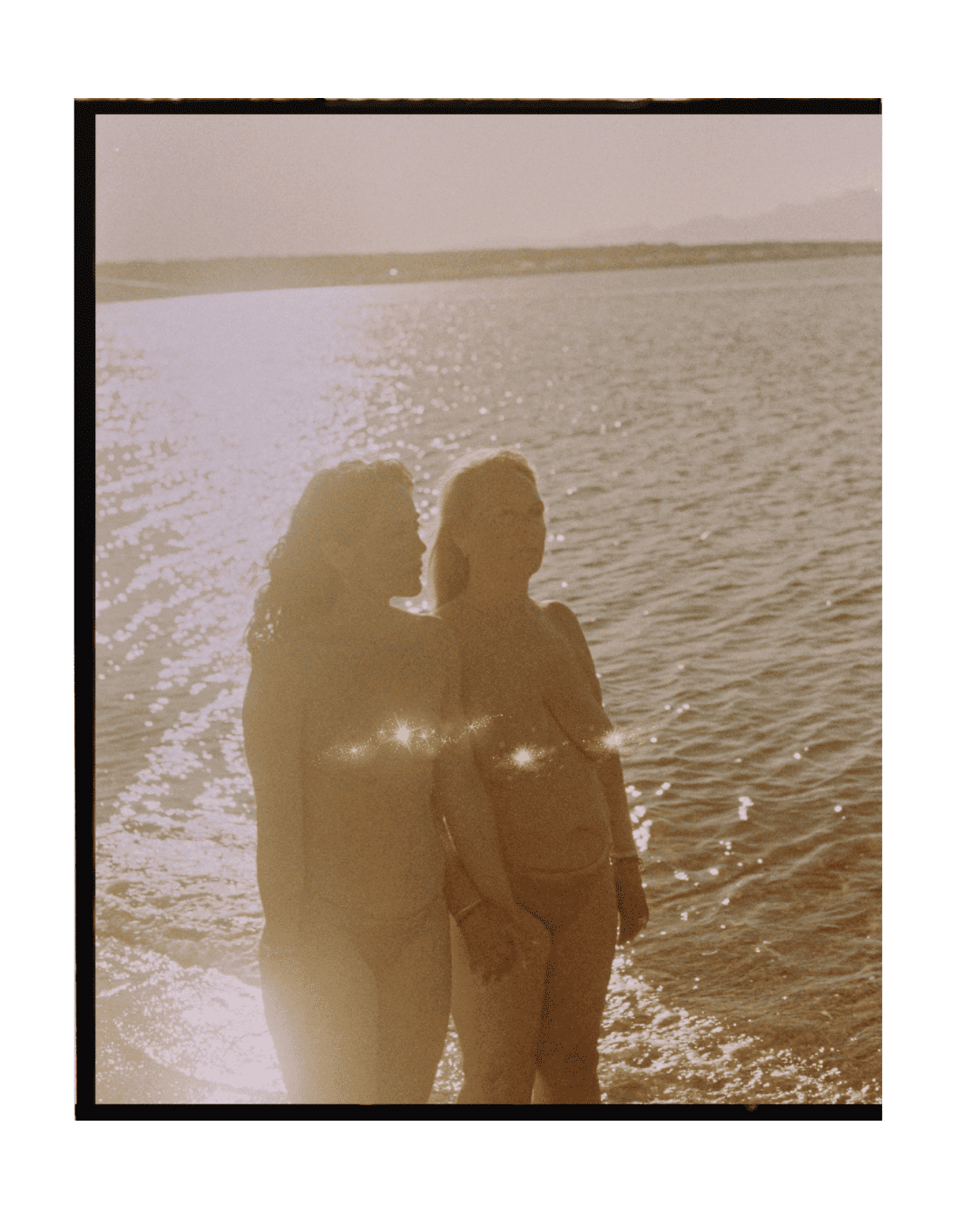 Dos mujeres tomando una fotografía en la playa durante el atardecer, en estilo vintage con reflejos de sol en el agua.