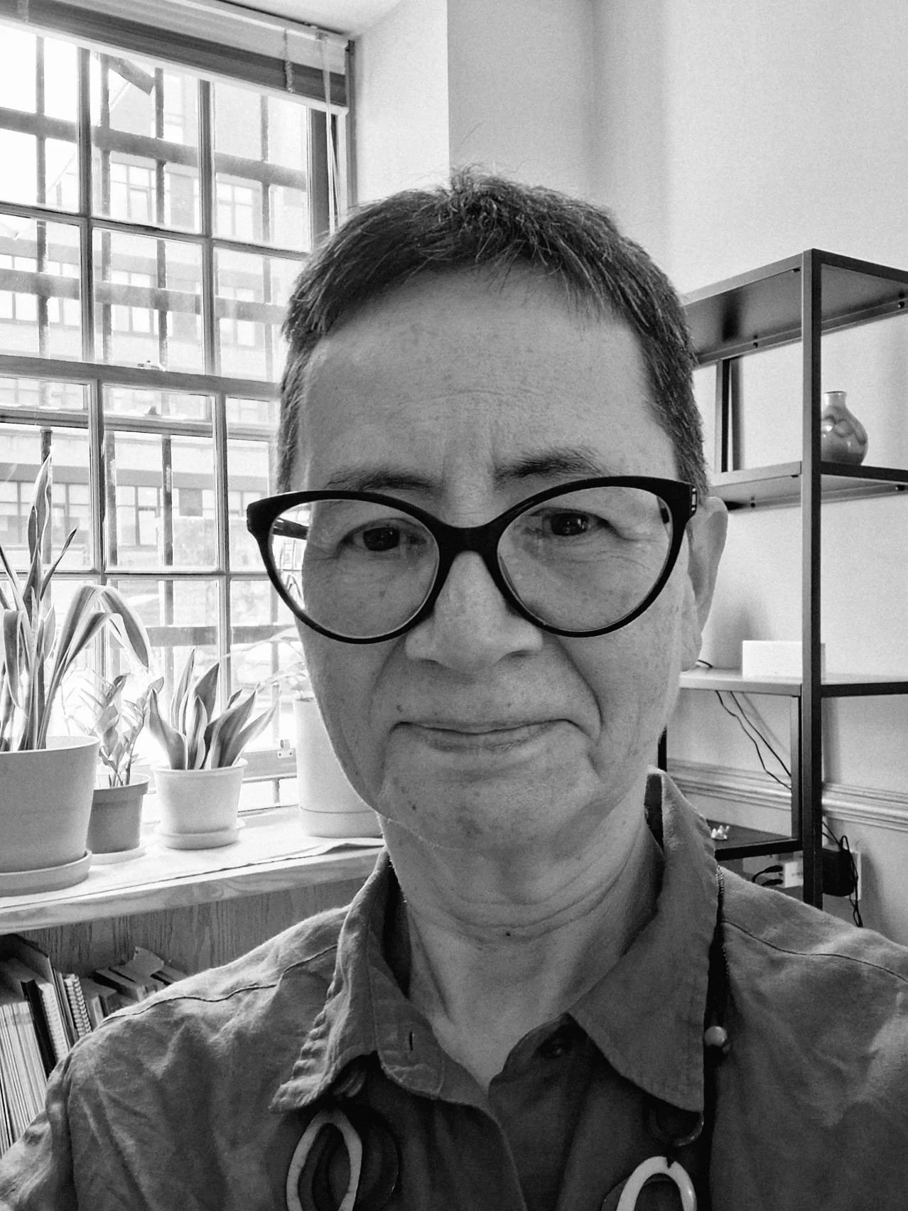 Black and white photo of a middle-aged man with glasses, smiling slightly, in an office setting with windows and houseplants in the background.