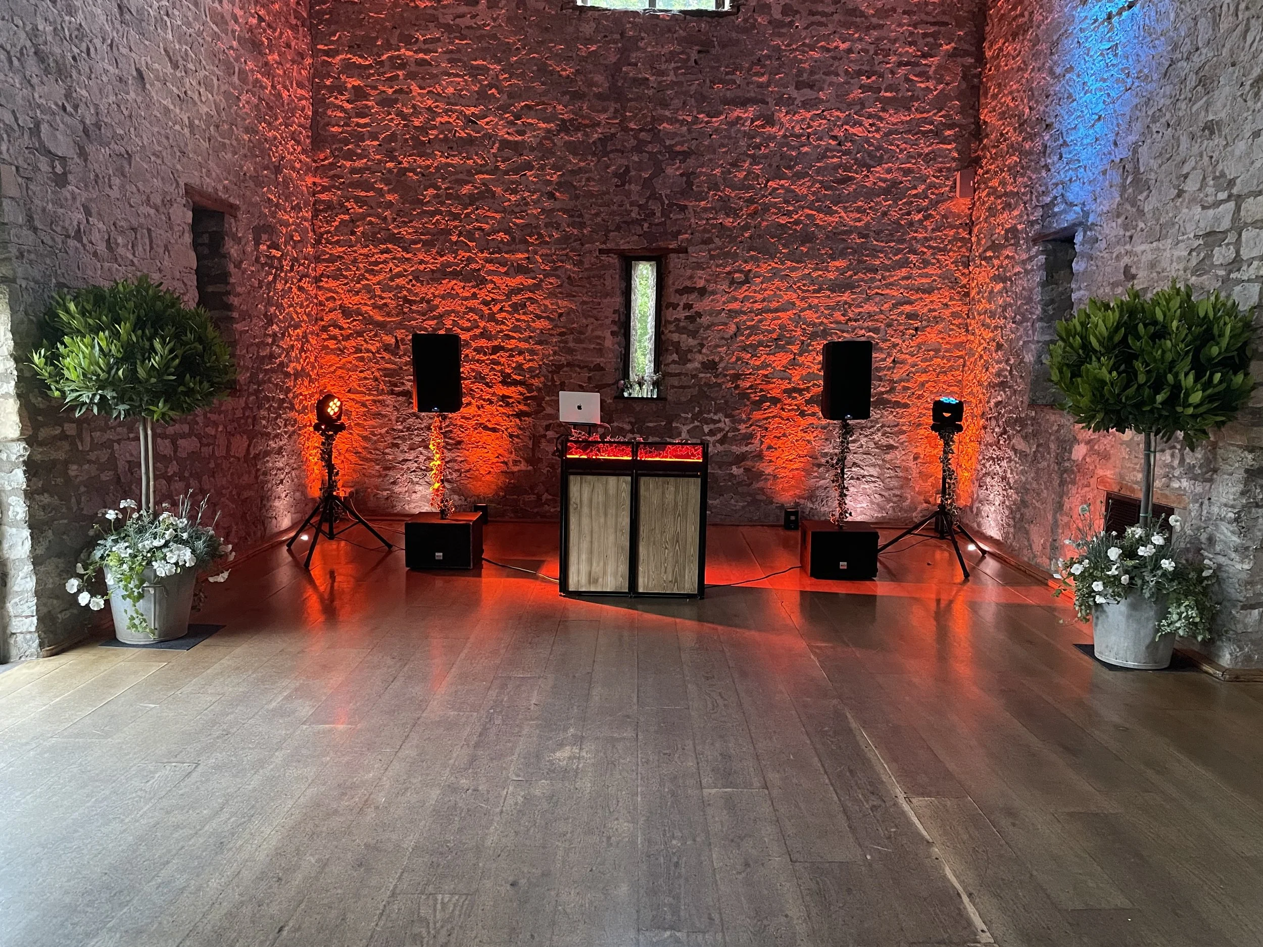 A stone-walled indoor space set up for an event or party with speakers, lighting, and decorative plants.