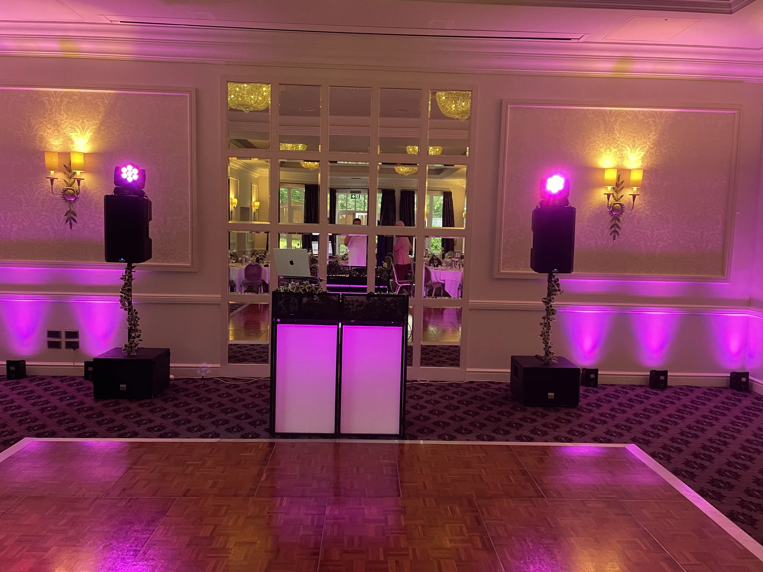 Empty dance floor with pink and purple lighting, large mirror wall, and tables set up for an event in the background.
