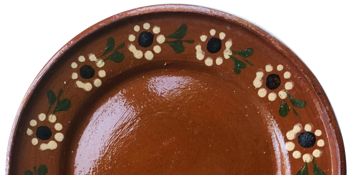 Close-up of a brown ceramic plate with a decorative floral pattern along the rim, consisting of white flowers with black centers and green leaves against a light blue background.