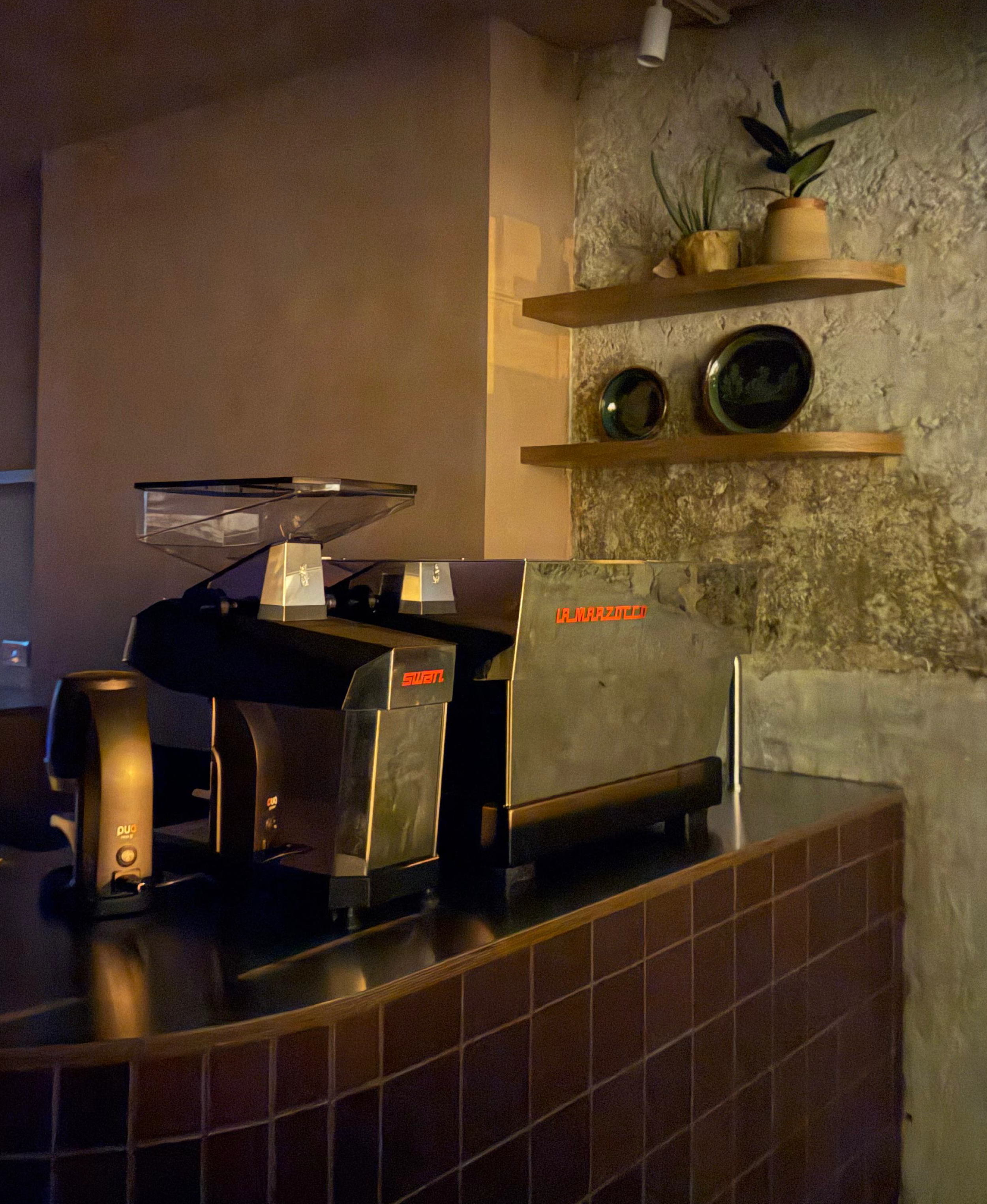 A barista counter, with a stone wall background and dark tiled lower wall.