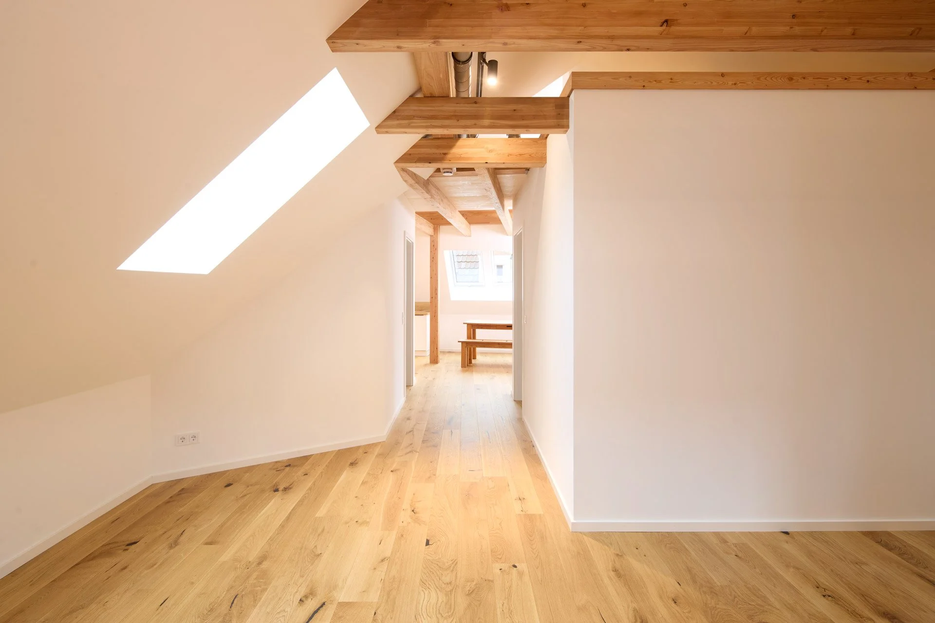 Innenraum eines Hauses mit Holzdecken, Holzboden und viel natürlichem Licht, durch große Fenster und Dachfenster.