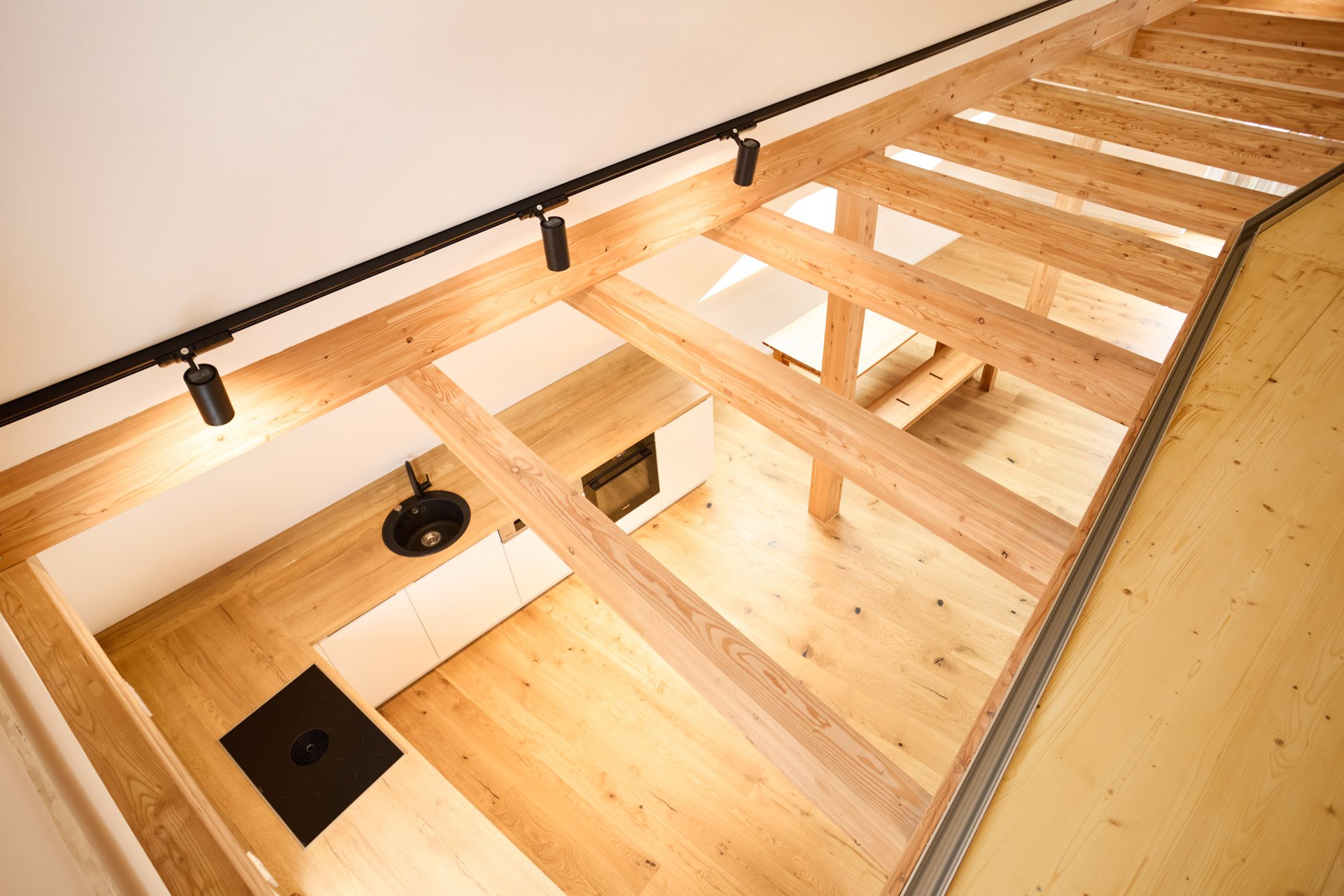 Innenaufnahme eines Hauses mit offener Holzdecke, weißer Küchenzeile, Herd, Spüle und Holzfußboden.