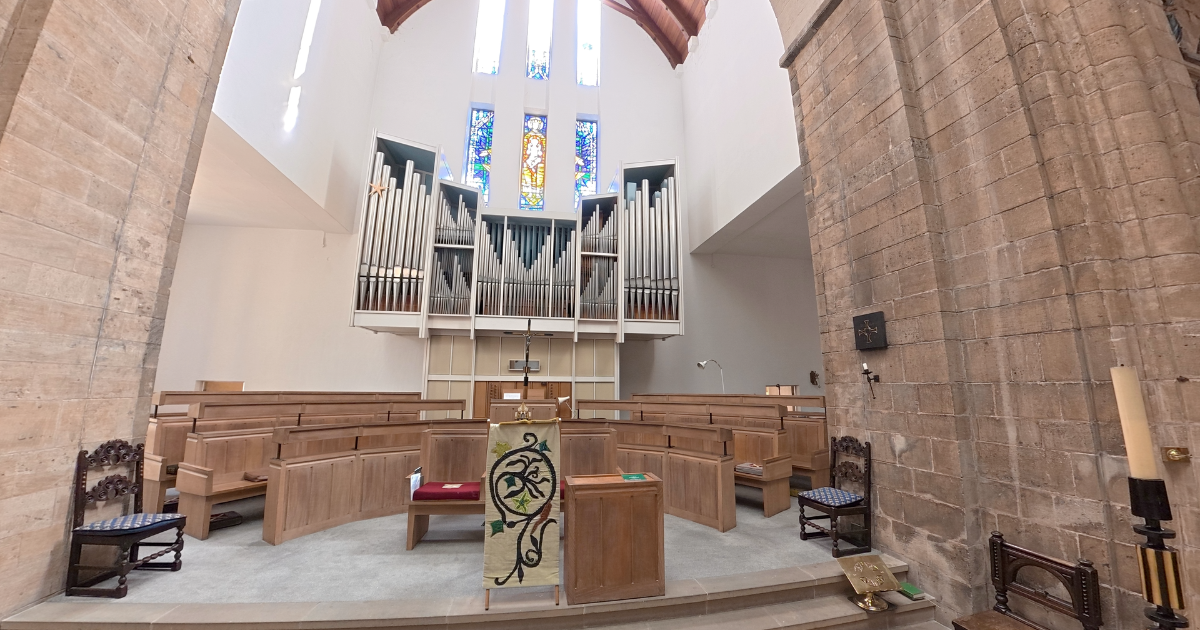 Interior of a church or chapel with wooden pews, an organ pipes, stained glass windows, and religious symbols.