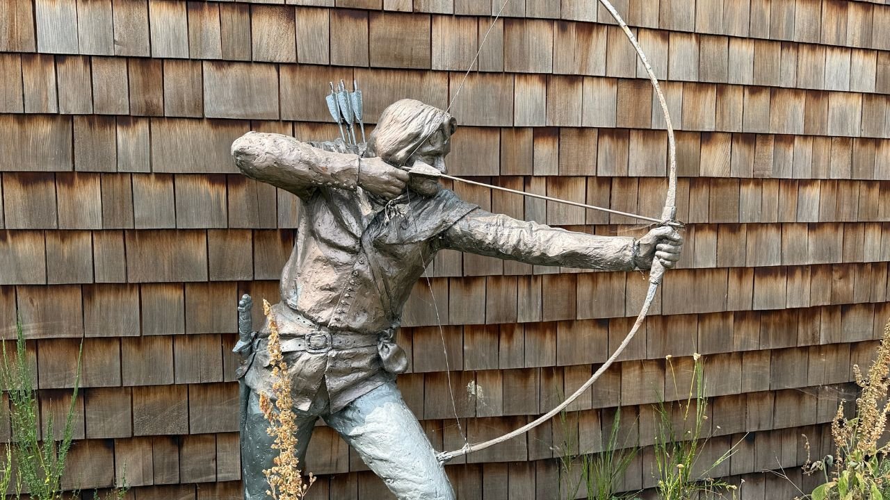 A bronze statue of a bow and arrow archer with a wartime backpack and ammunition on the back, aiming the bow.