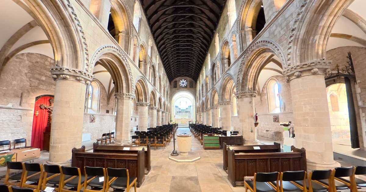 Interior of a church with stone columns, arches, and stained glass windows, arranged for a service with chairs and an altar at the front.
