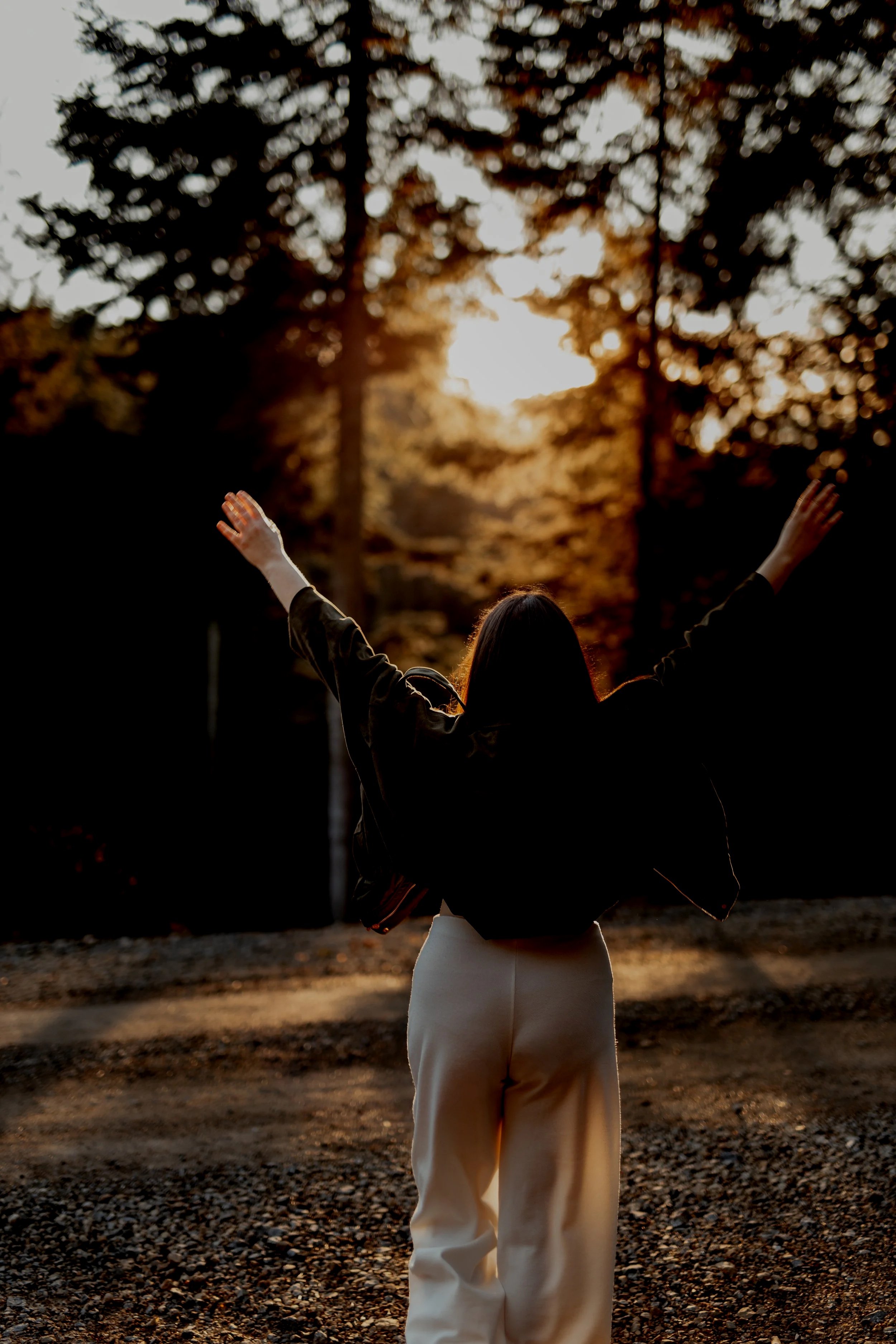 Eine Person mit offenen Armen, Blick auf einen Sonnenuntergang im Wald.